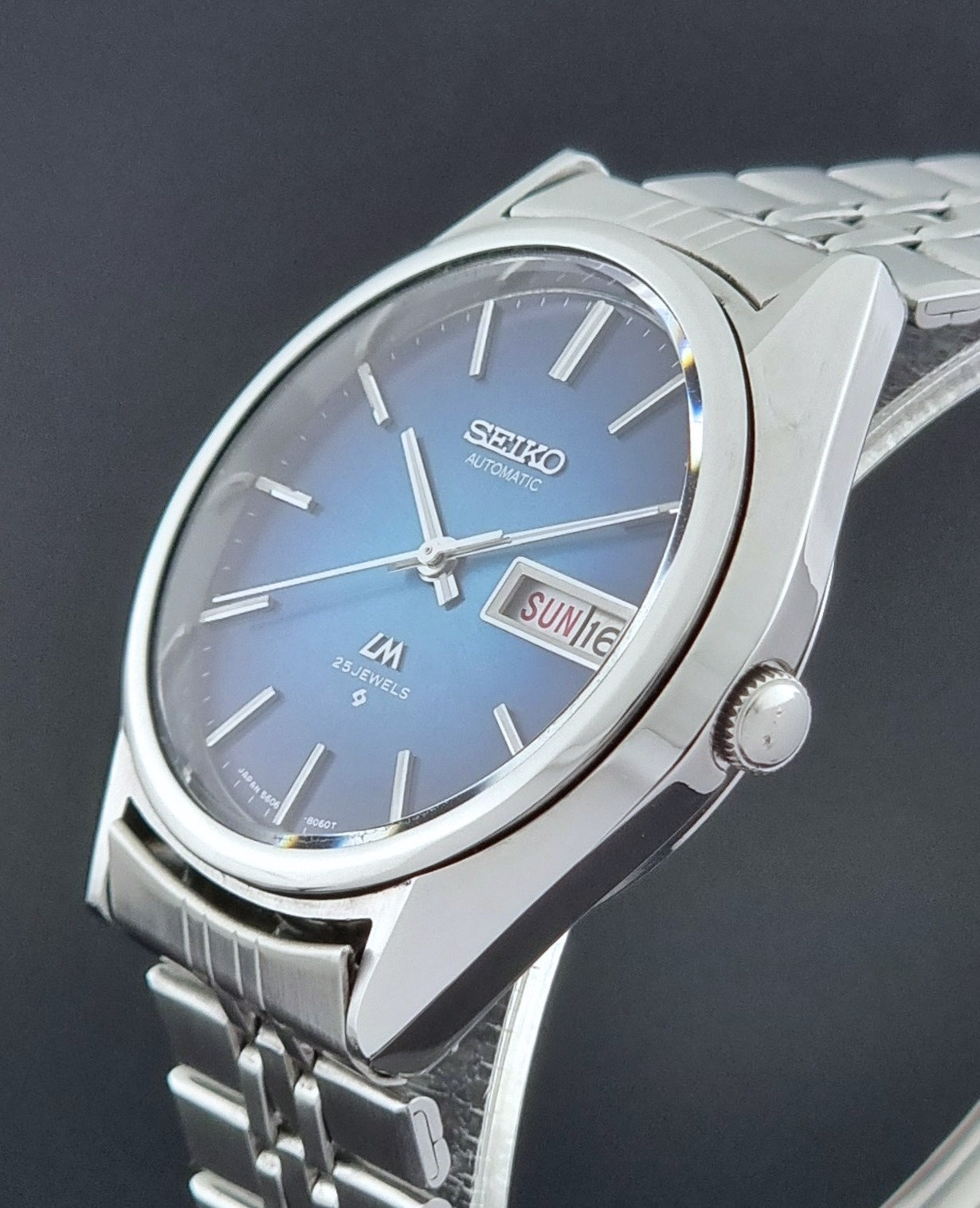Vintage Seiko Wristwatch LordMatic 5606-8030 with blue gradient dial on a dark textured surface crown view