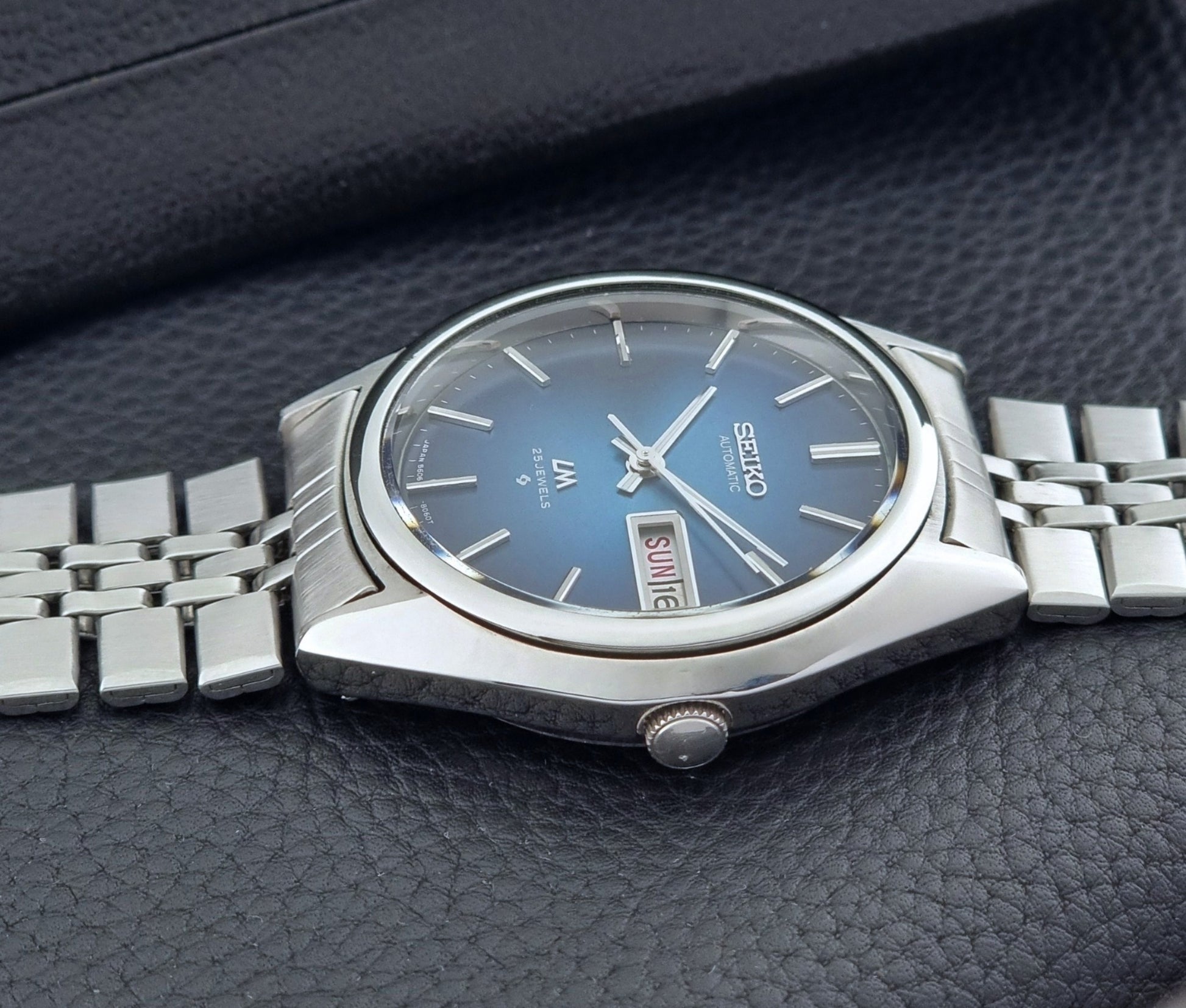 Vintage Seiko Wristwatch LordMatic 5606-8030 with blue gradient dial on a dark textured surface side profile view