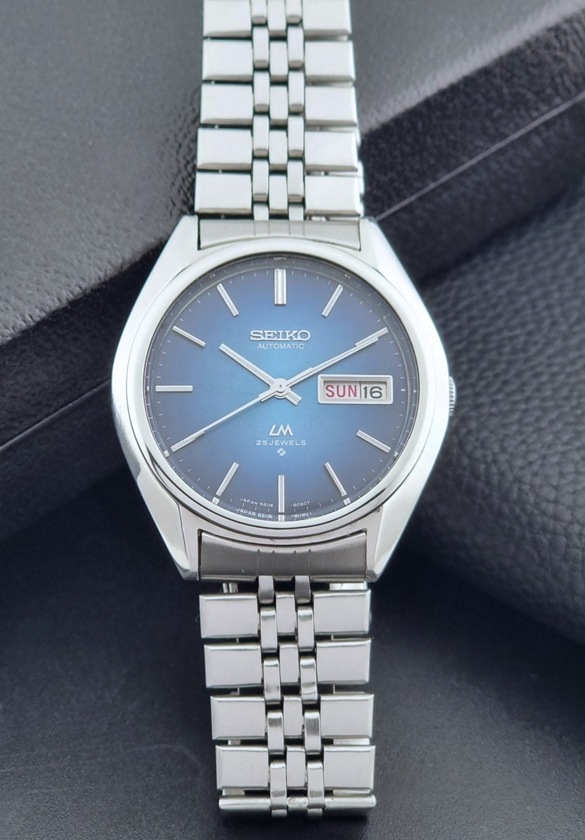 Vintage Seiko Wristwatch LordMatic 5606-8030 with blue gradient dial on a dark textured surface front view