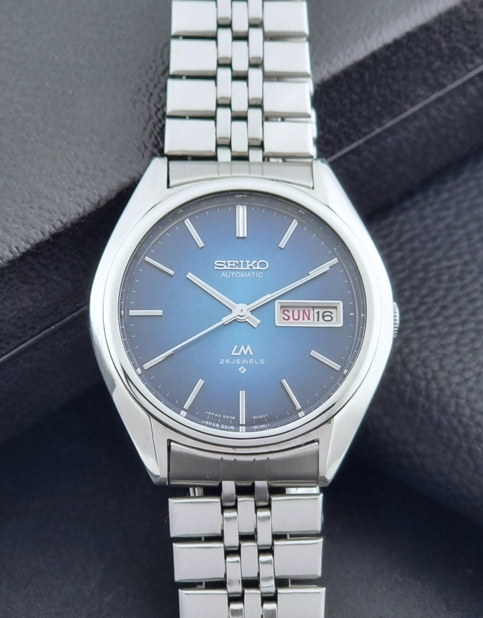 Vintage Seiko Wristwatch LordMatic 5606-8030 with blue gradient dial on a dark textured surface dial view