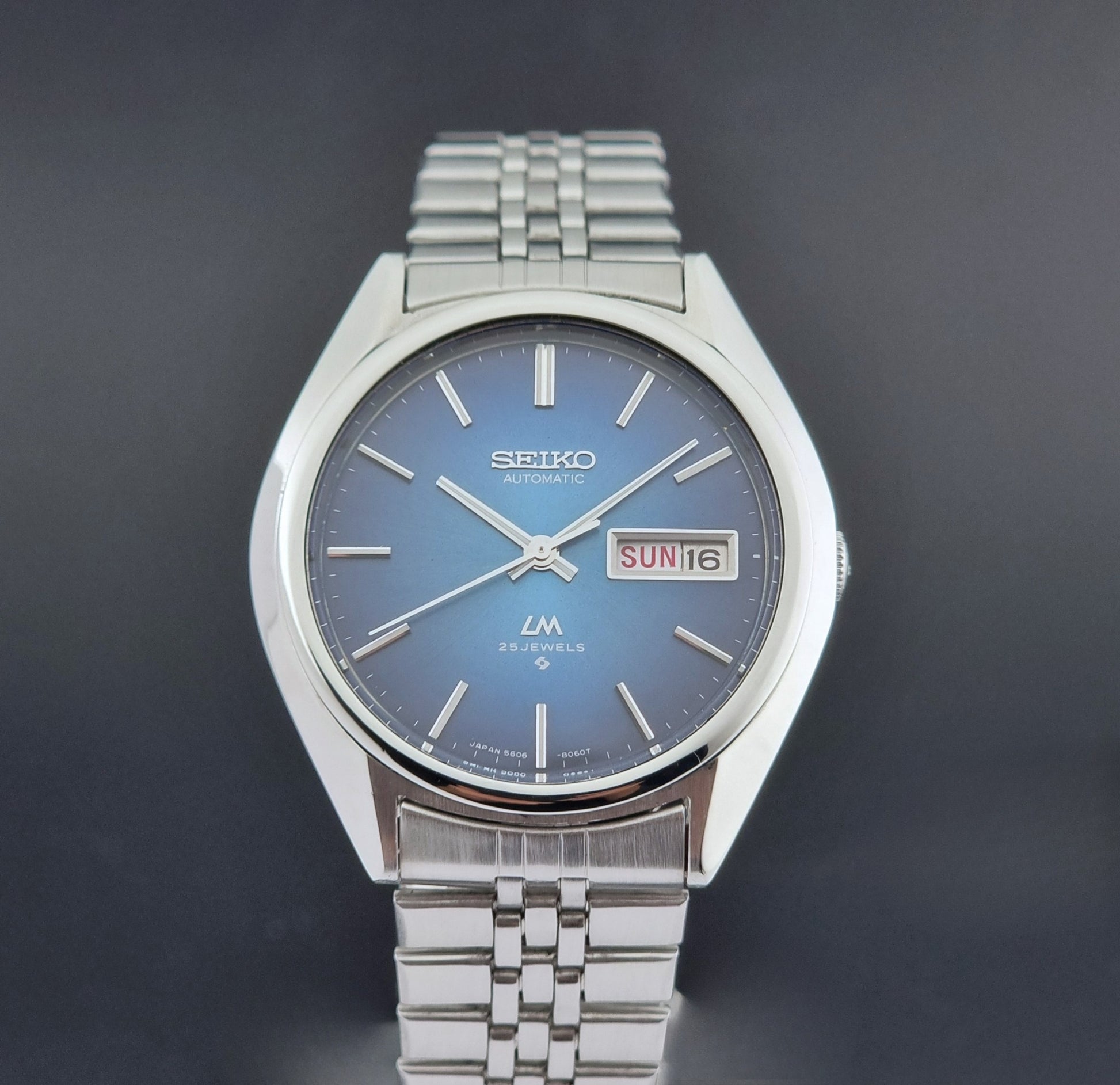 Vintage Seiko Wristwatch LordMatic 5606-8030 with blue gradient dial on a dark textured surface close up dial view