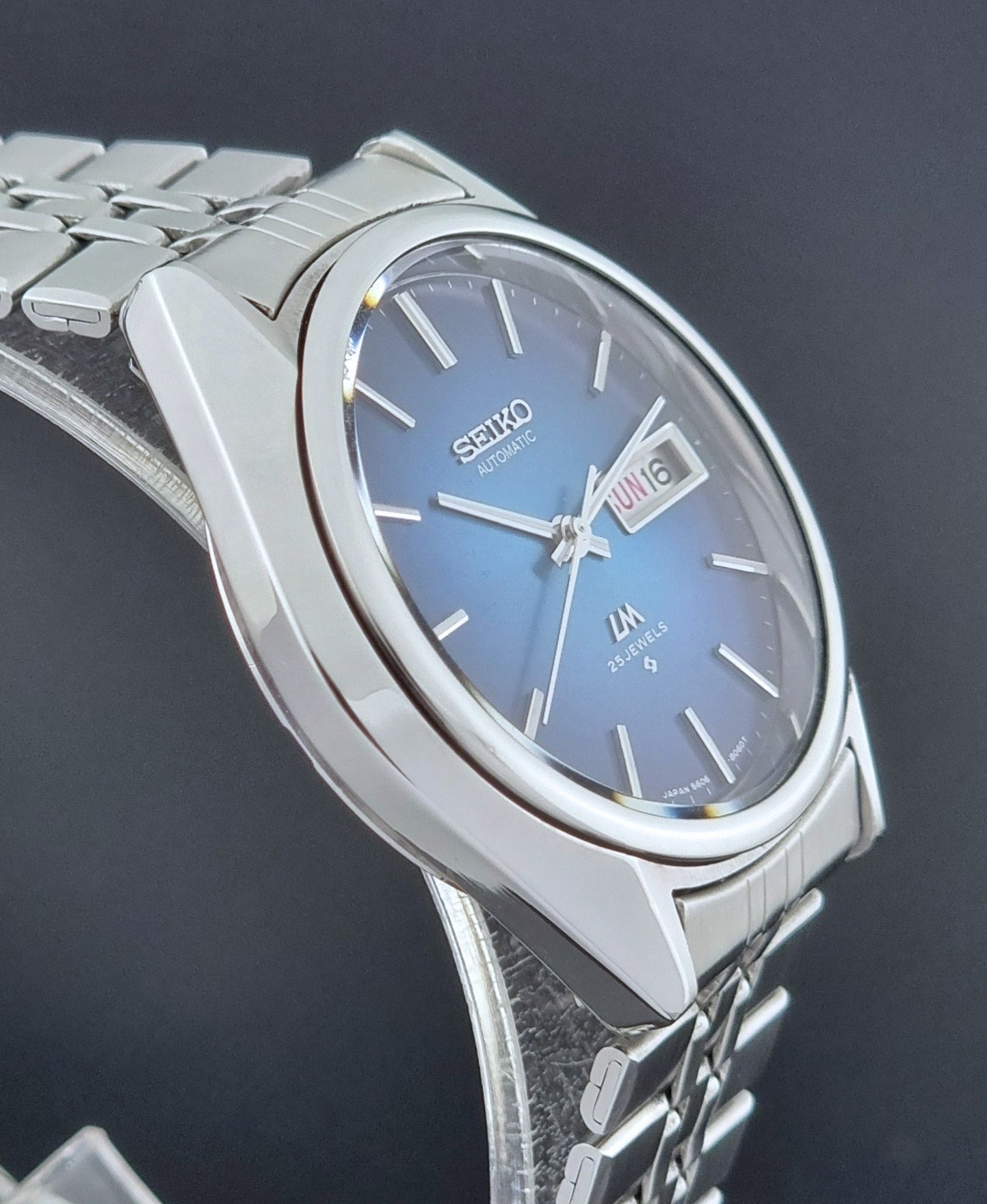 Vintage Seiko Wristwatch LordMatic 5606-8030 with blue gradient dial on a dark textured surface side view