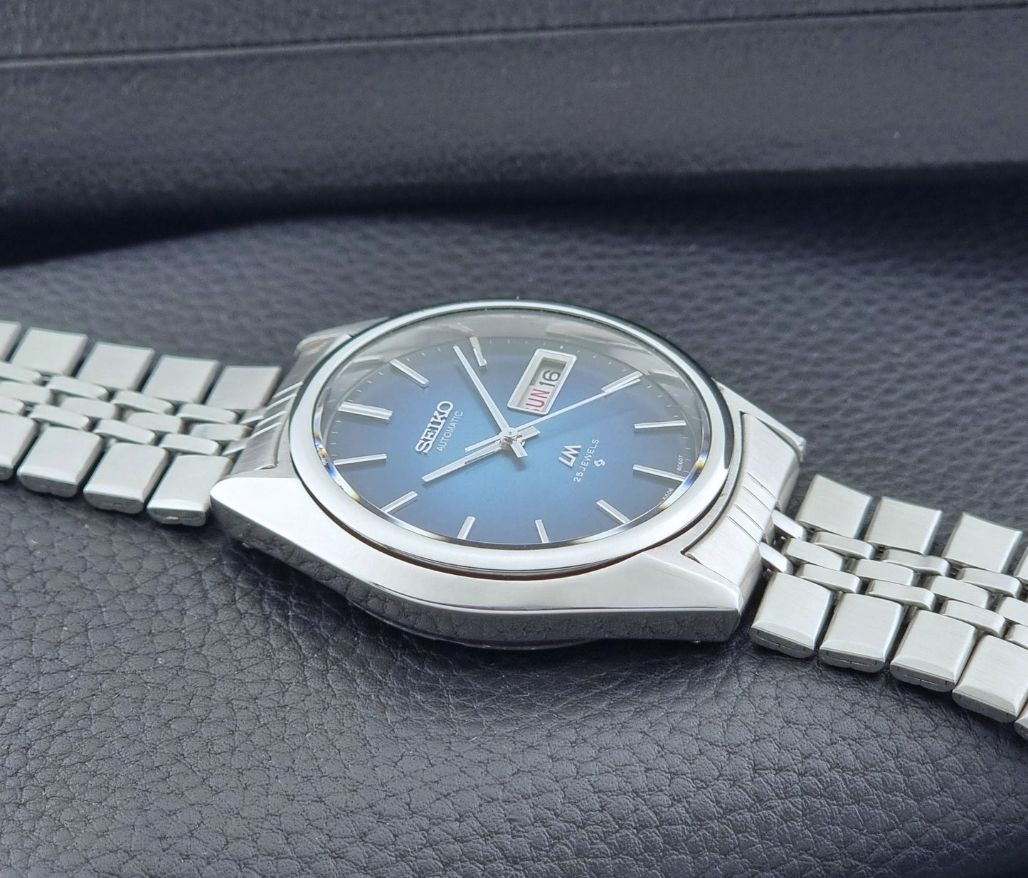 Vintage Seiko Wristwatch LordMatic 5606-8030 with blue gradient dial on a dark textured surface crown profile view