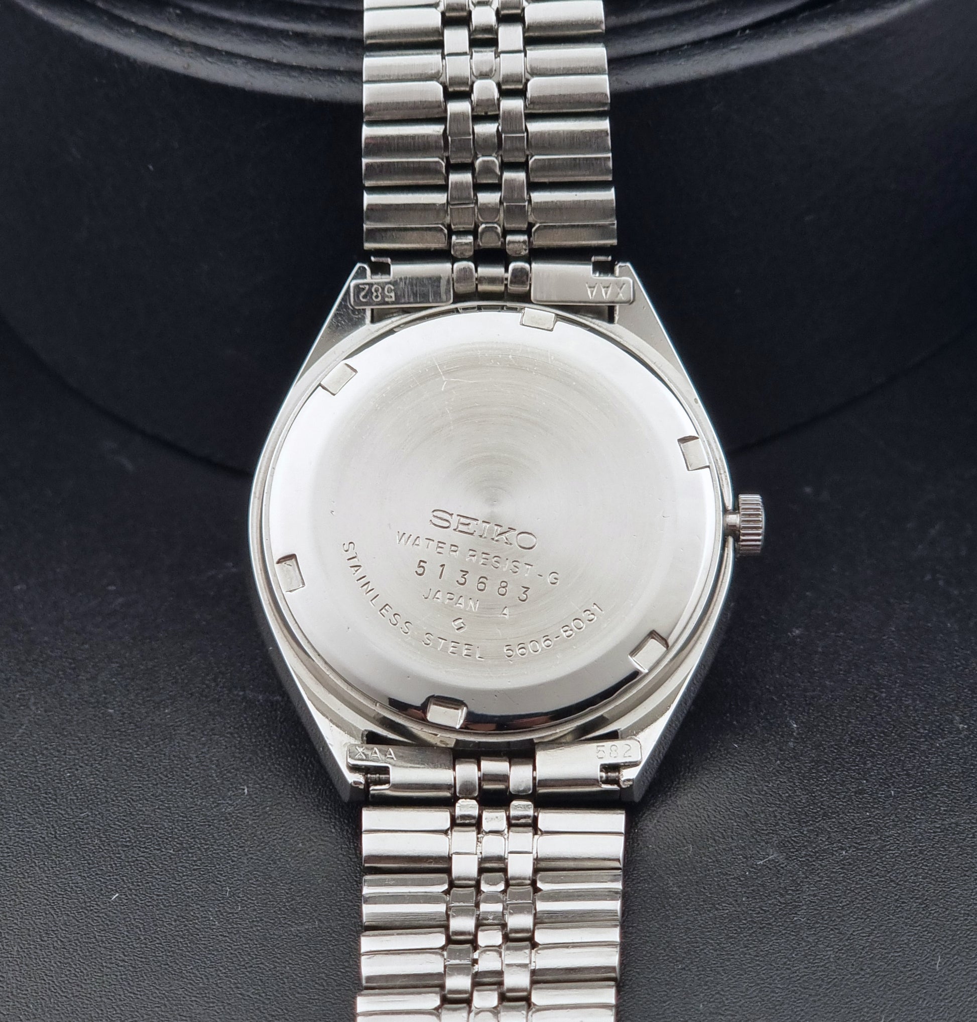 The back of a stainless steel Vintage Seiko watch LordMatic 5606-8031 with a metal link bracelet, photographed close-up against a dark textured background.