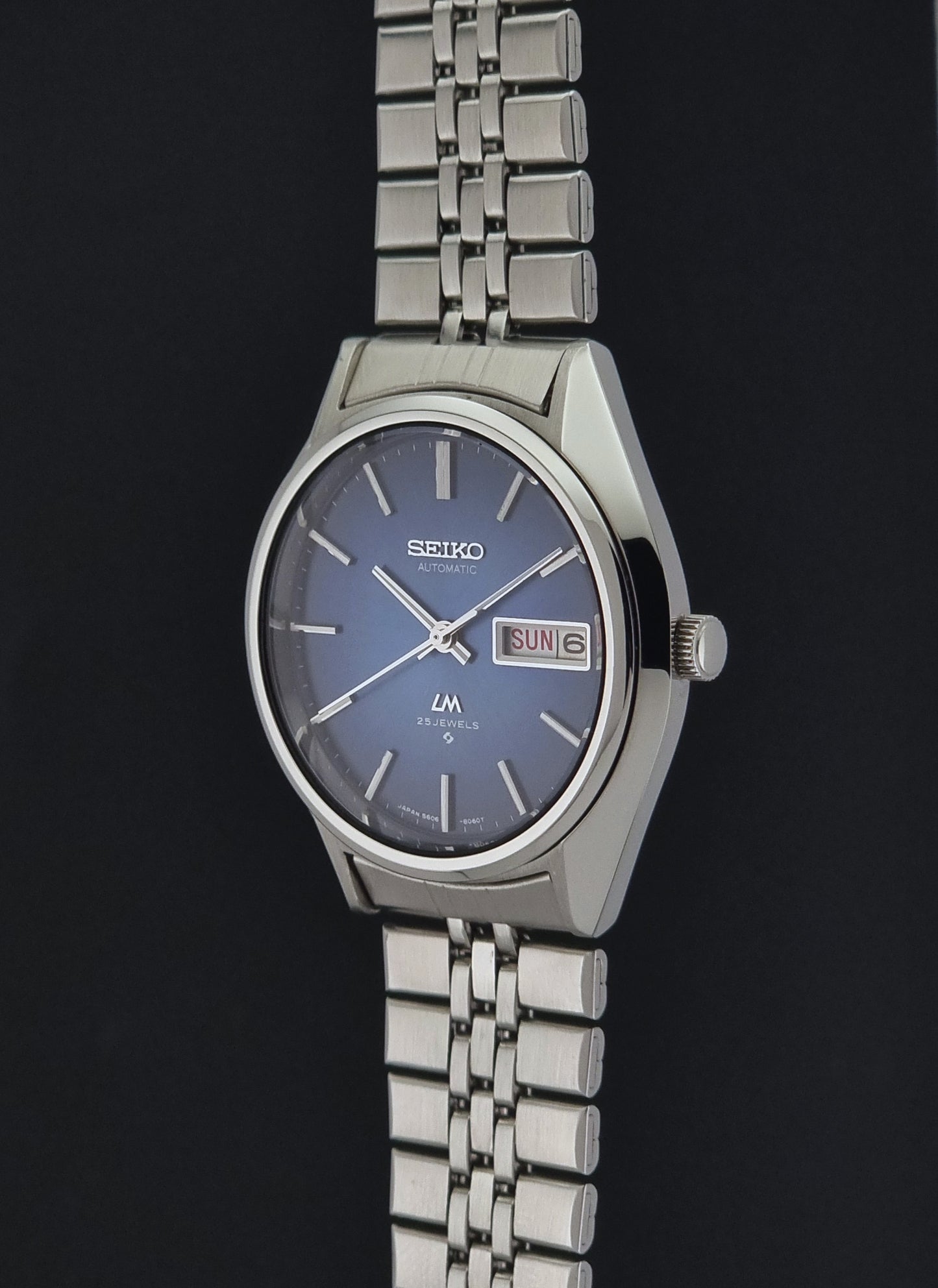 A Vintage Seiko watch LordMatic 5606-8031 featuring a silver stainless steel case and link bracelet, with a blue dial and a day-date window.