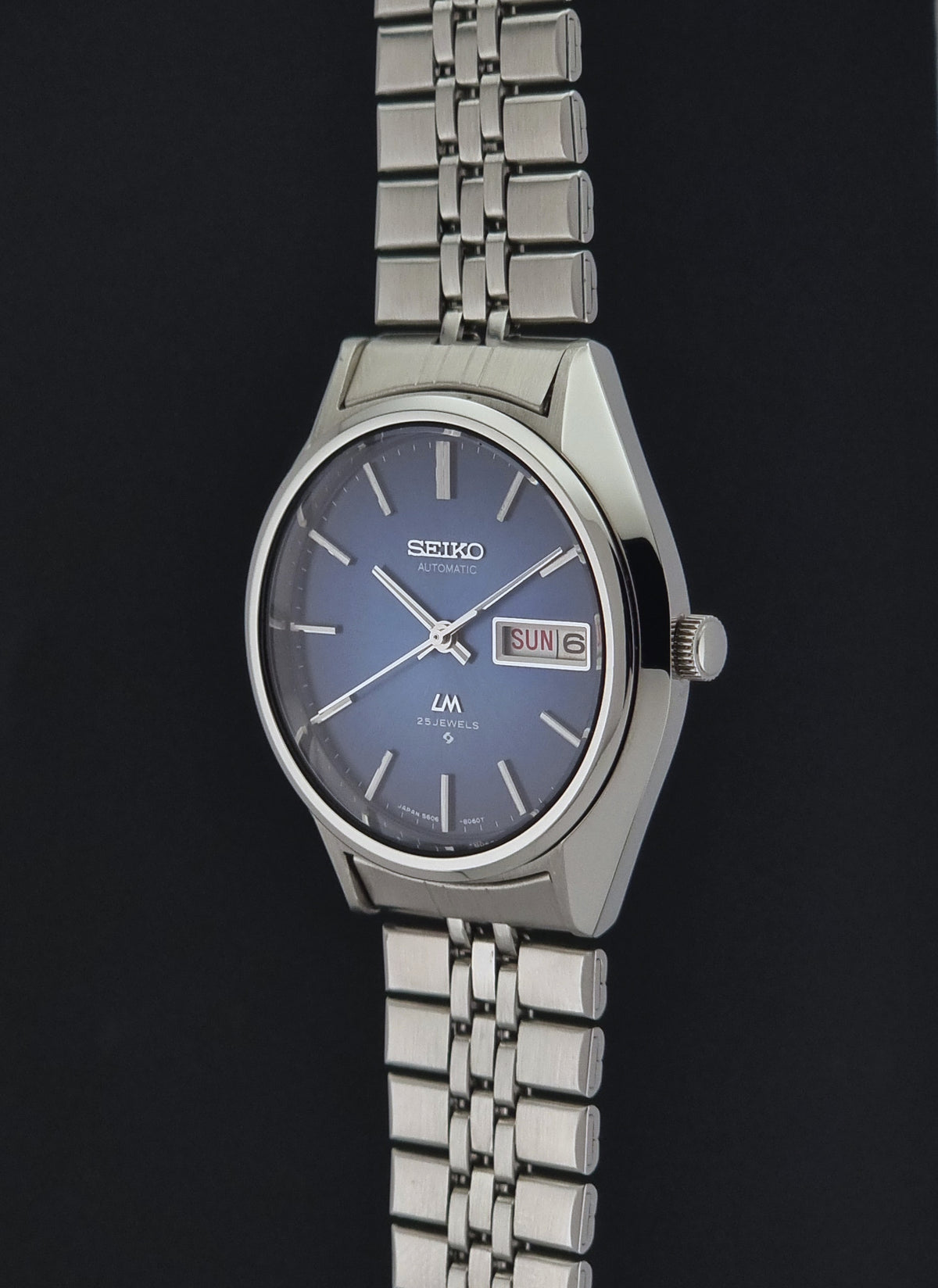 A Vintage Seiko watch LordMatic 5606-8031 featuring a silver stainless steel case and link bracelet, with a blue dial and a day-date window.