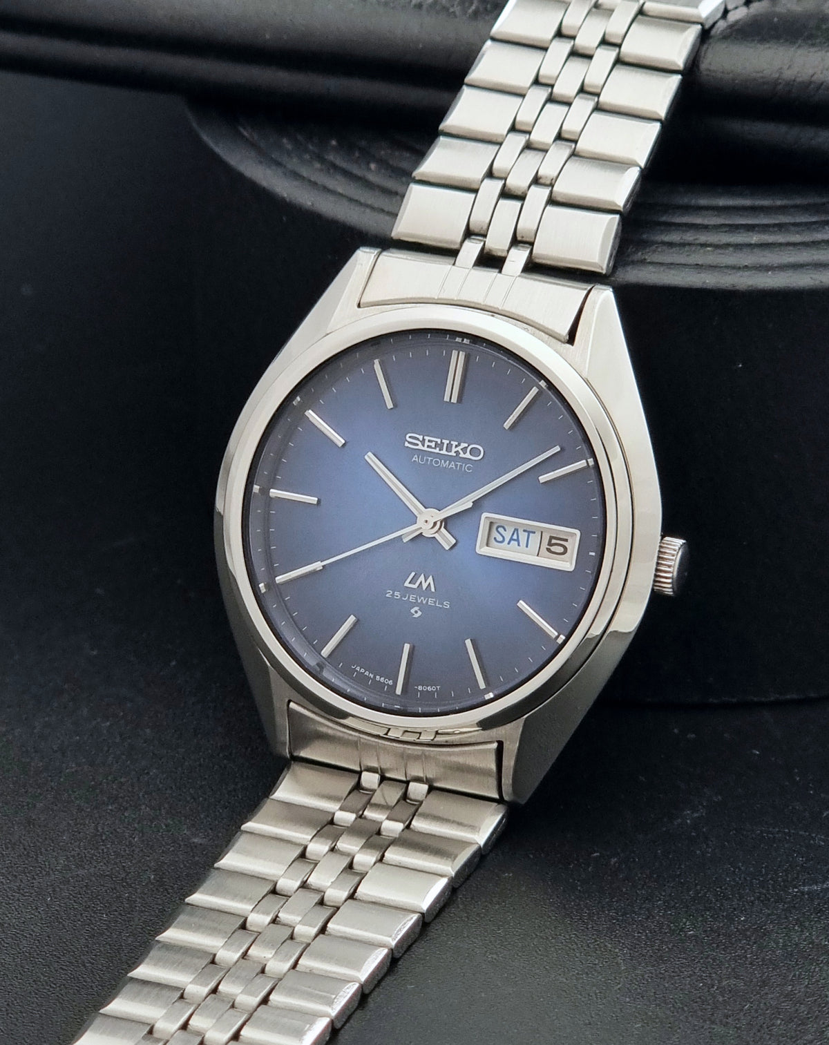 A Vintage Seiko watch LordMatic 5606-8031 Automatic watch with a silver stainless steel case and link bracelet, featuring a blue dial with silver indices and a day-date window.