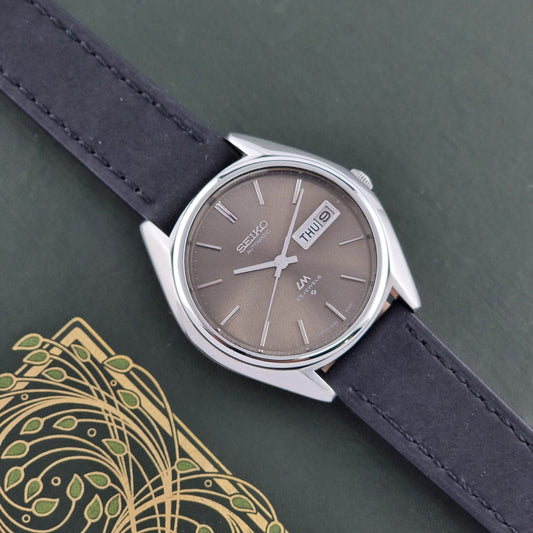 Vintage Seiko Lordmatic 5606-8031 watch with a brown dial and a dark strap on a green background