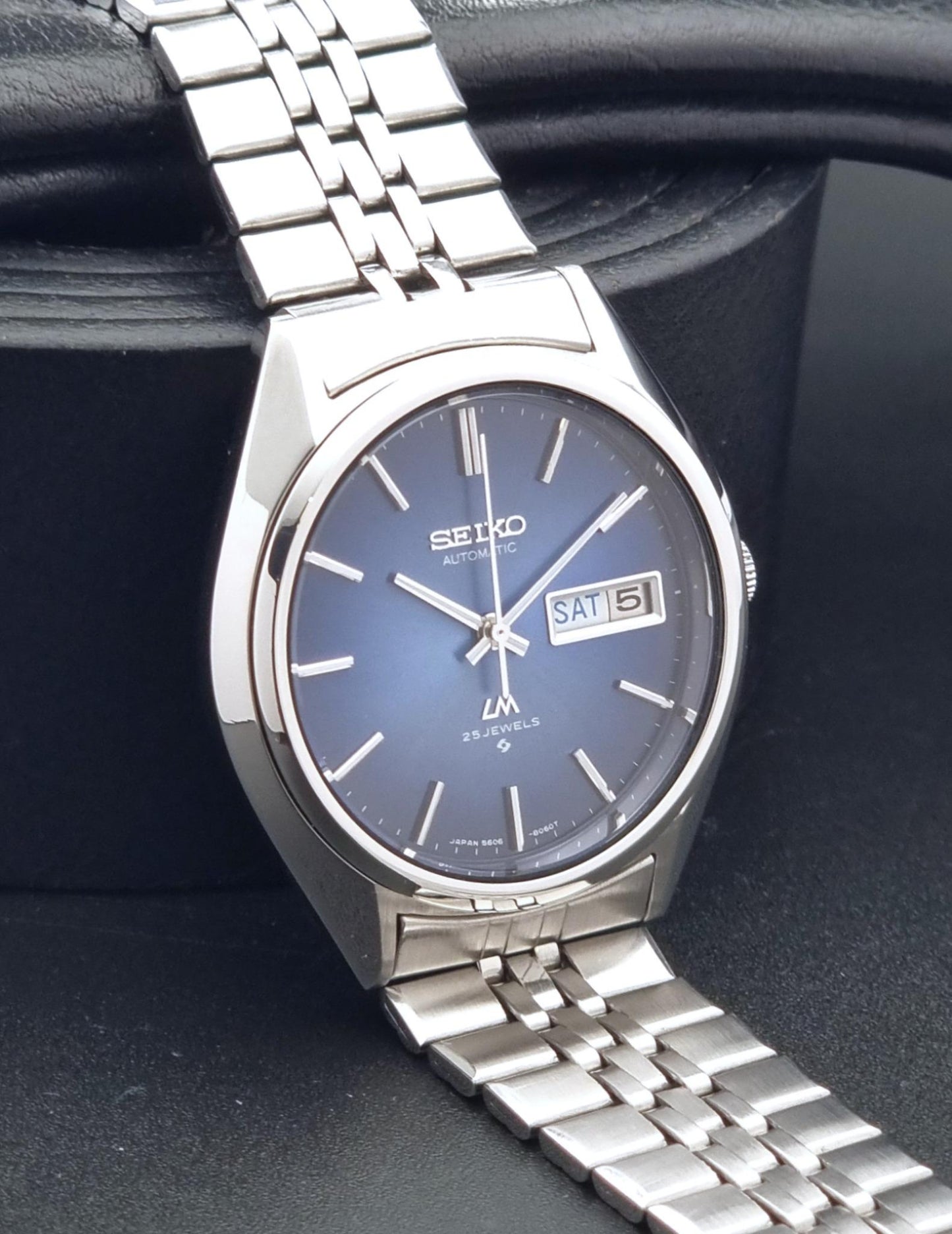 A Vintage Seiko watch LordMatic 5606-8031 with a silver stainless steel case and link bracelet, featuring a blue sunburst dial with a day and date window.