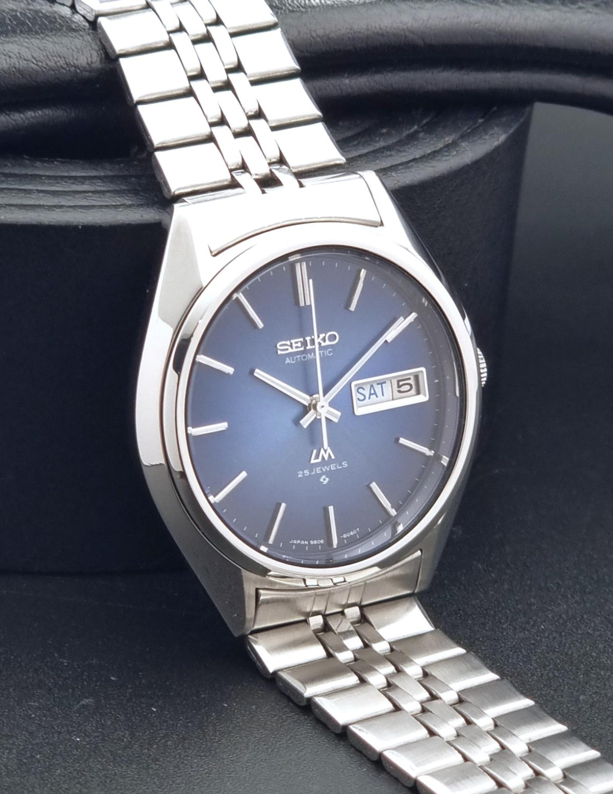A Vintage Seiko watch LordMatic 5606-8031 with a silver stainless steel case and link bracelet, featuring a blue sunburst dial with a day and date window.