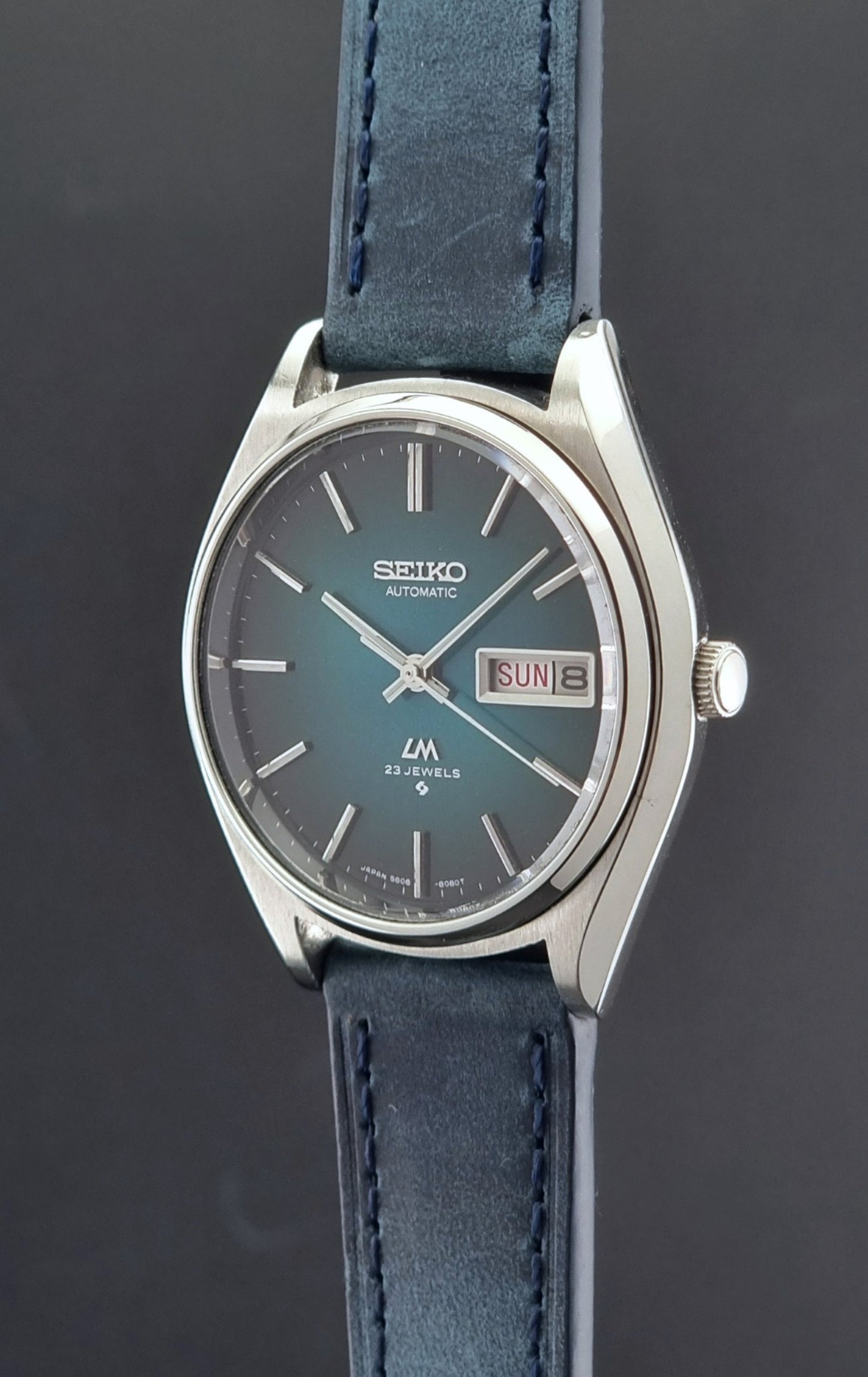 Vintage Seiko watch LordMatic 5606-8050 with blue leather strap on a dark gray background crown side profile view