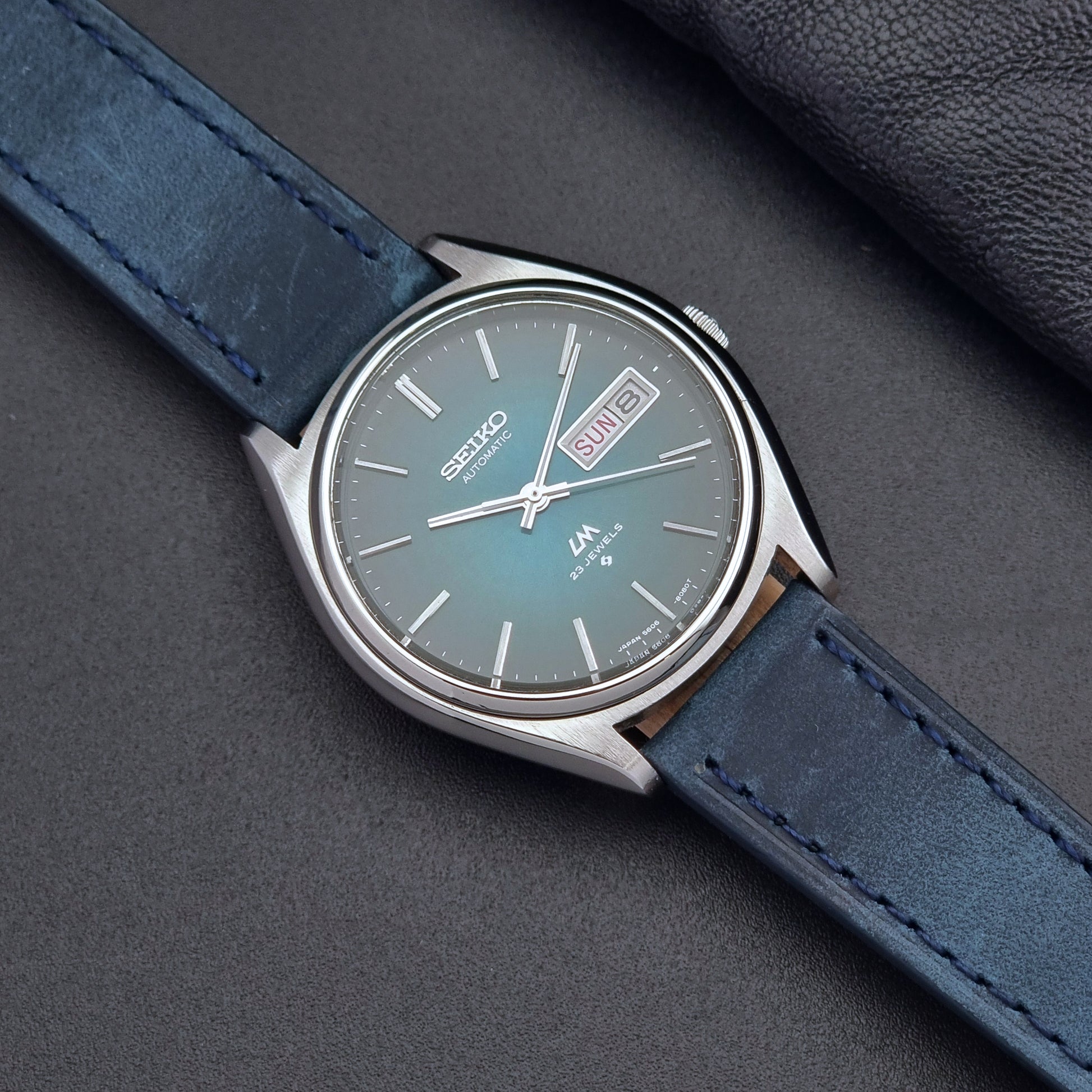 Vintage Seiko watch LordMatic 5606-8050 with blue leather strap on a dark gray background
