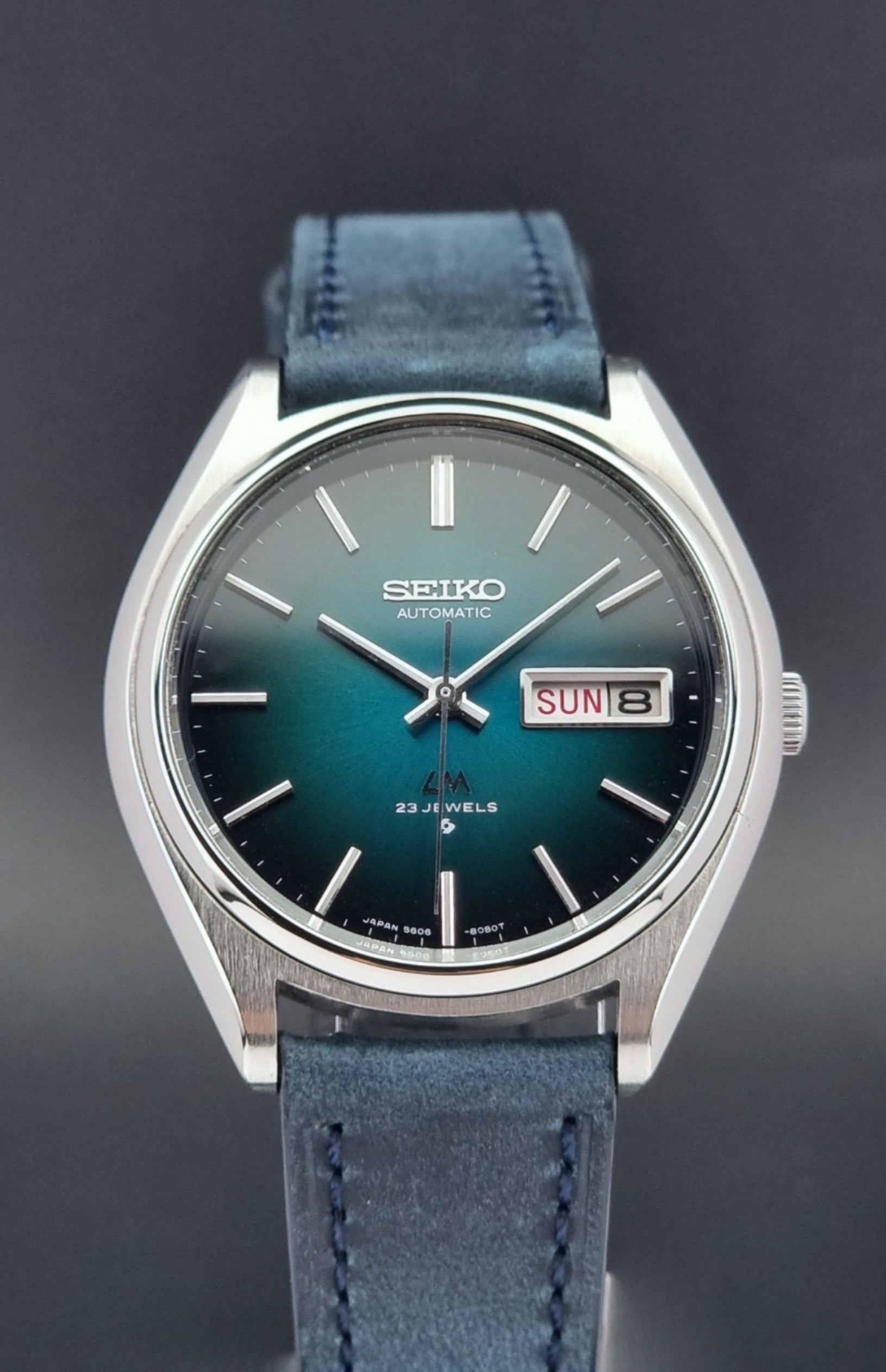 Vintage Seiko watch LordMatic 5606-8050 with blue leather strap on a dark gray background front view