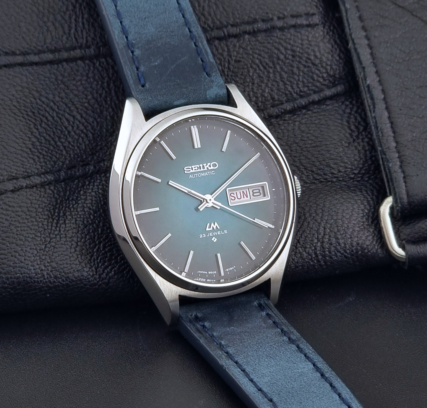 Vintage Seiko watch LordMatic 5606-8050 with blue leather strap on a dark gray background side view