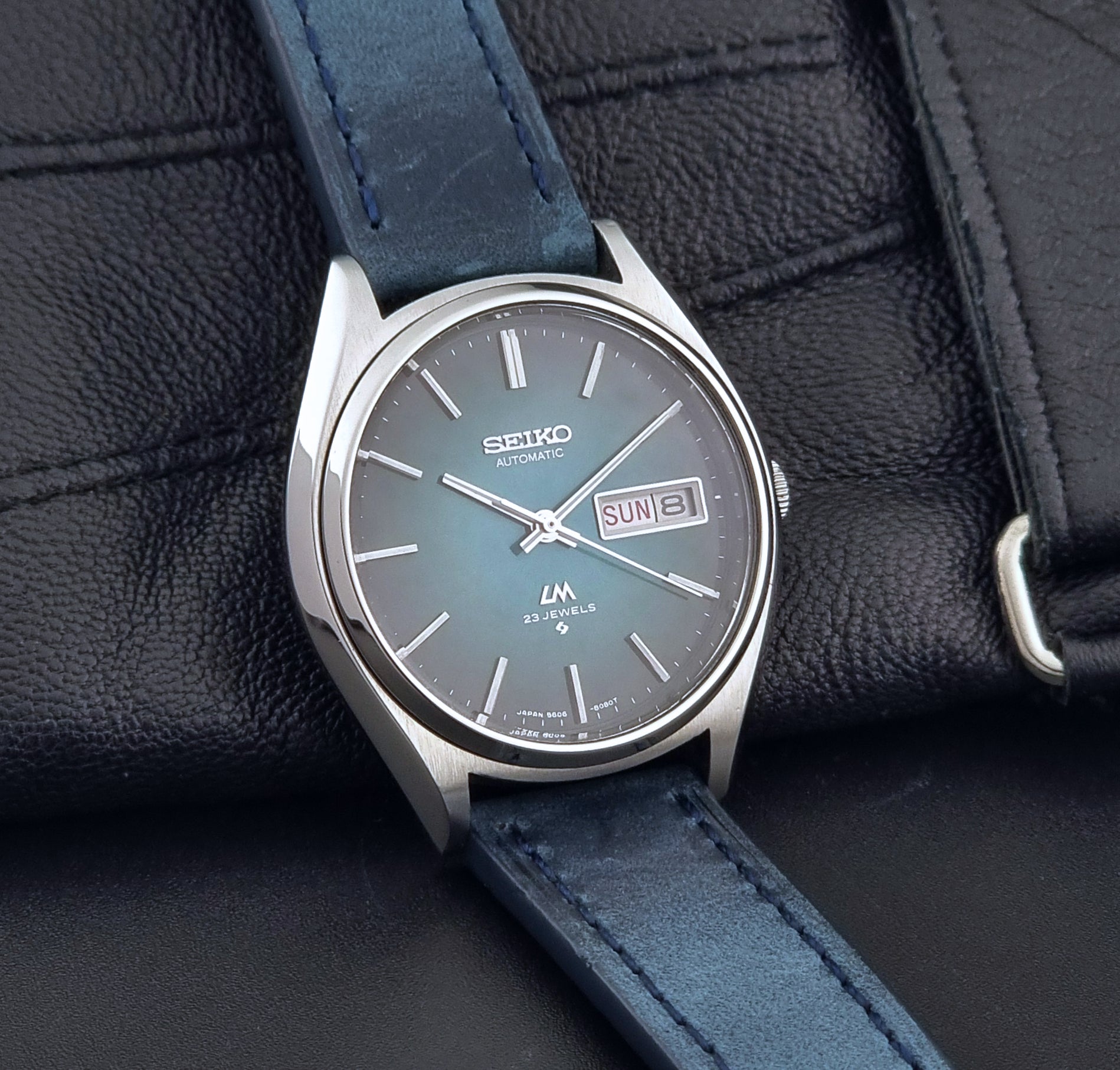 Vintage Seiko watch LordMatic 5606-8050 with blue leather strap on a dark gray background side view