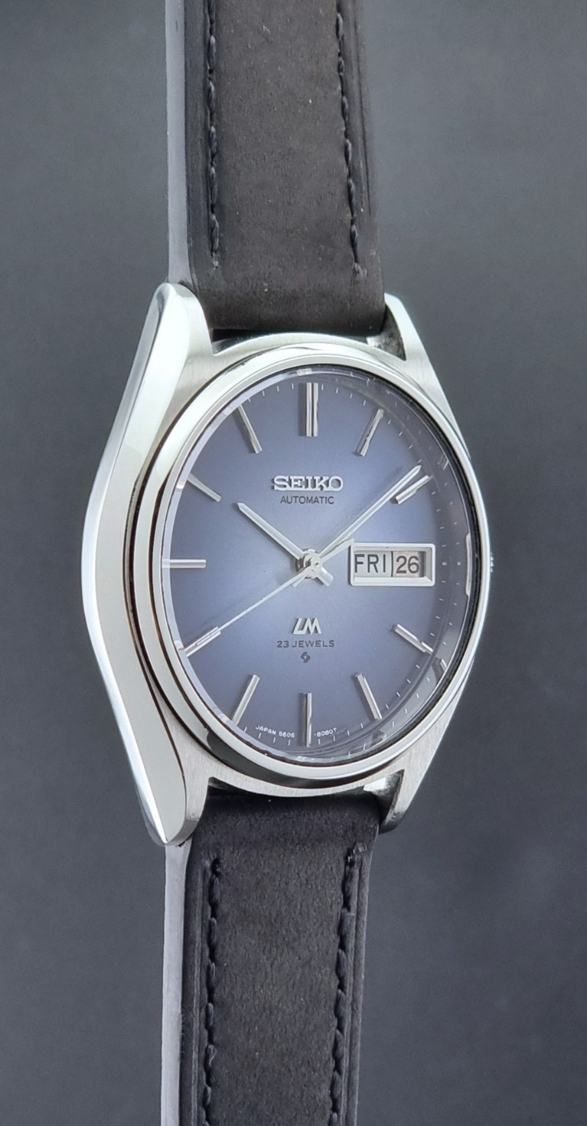 Vintage Seiko Wristwatch LordMatic 5606-8050 with blue gradient dial on a dark surface side profile view