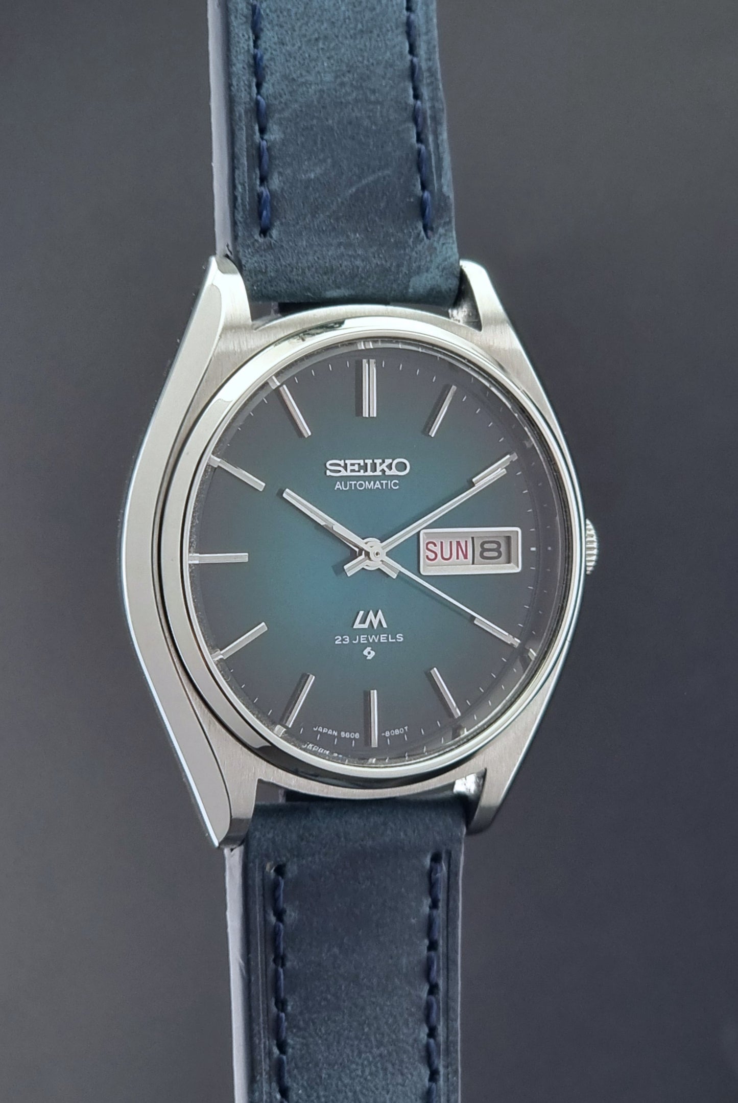 Vintage Seiko watch LordMatic 5606-8050 with blue leather strap on a dark gray background side profile