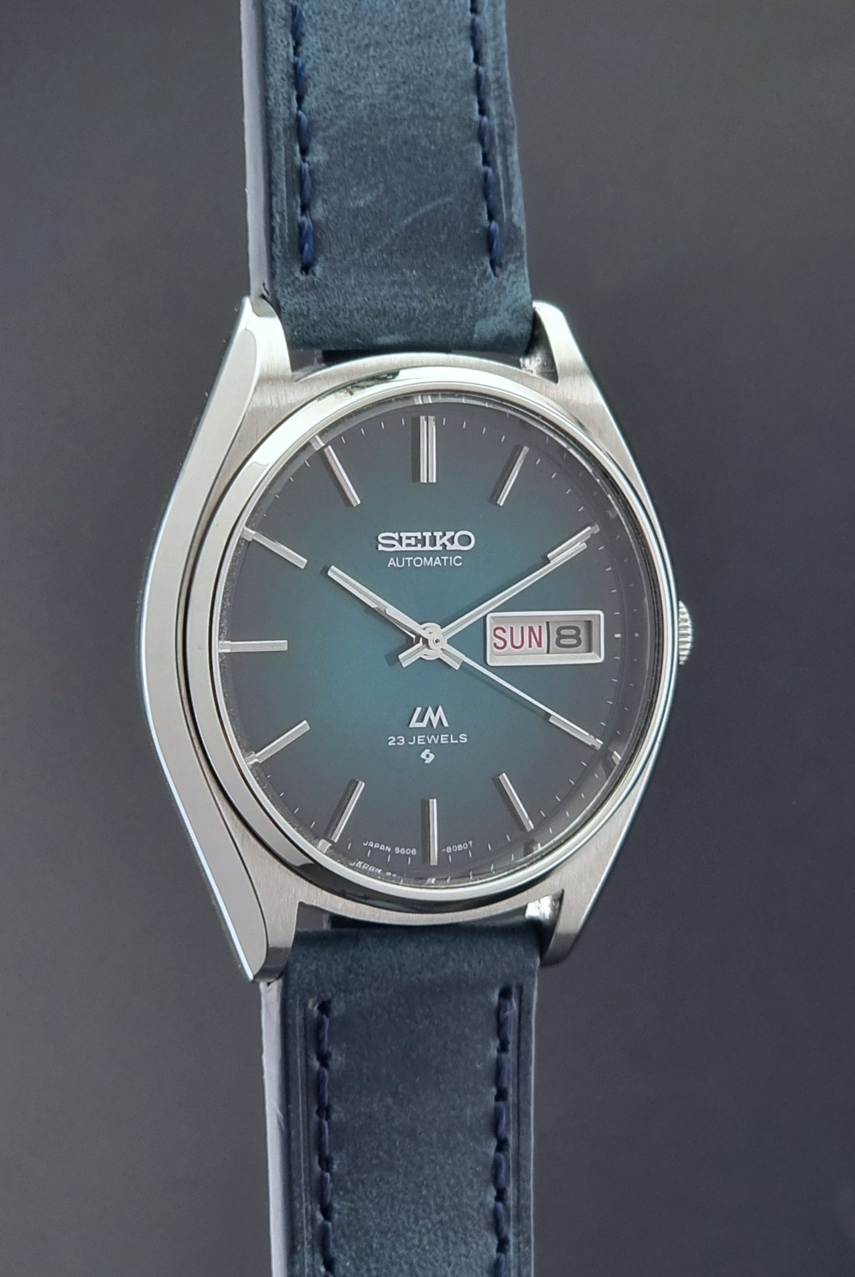 Vintage Seiko watch LordMatic 5606-8050 with blue leather strap on a dark gray background side profile