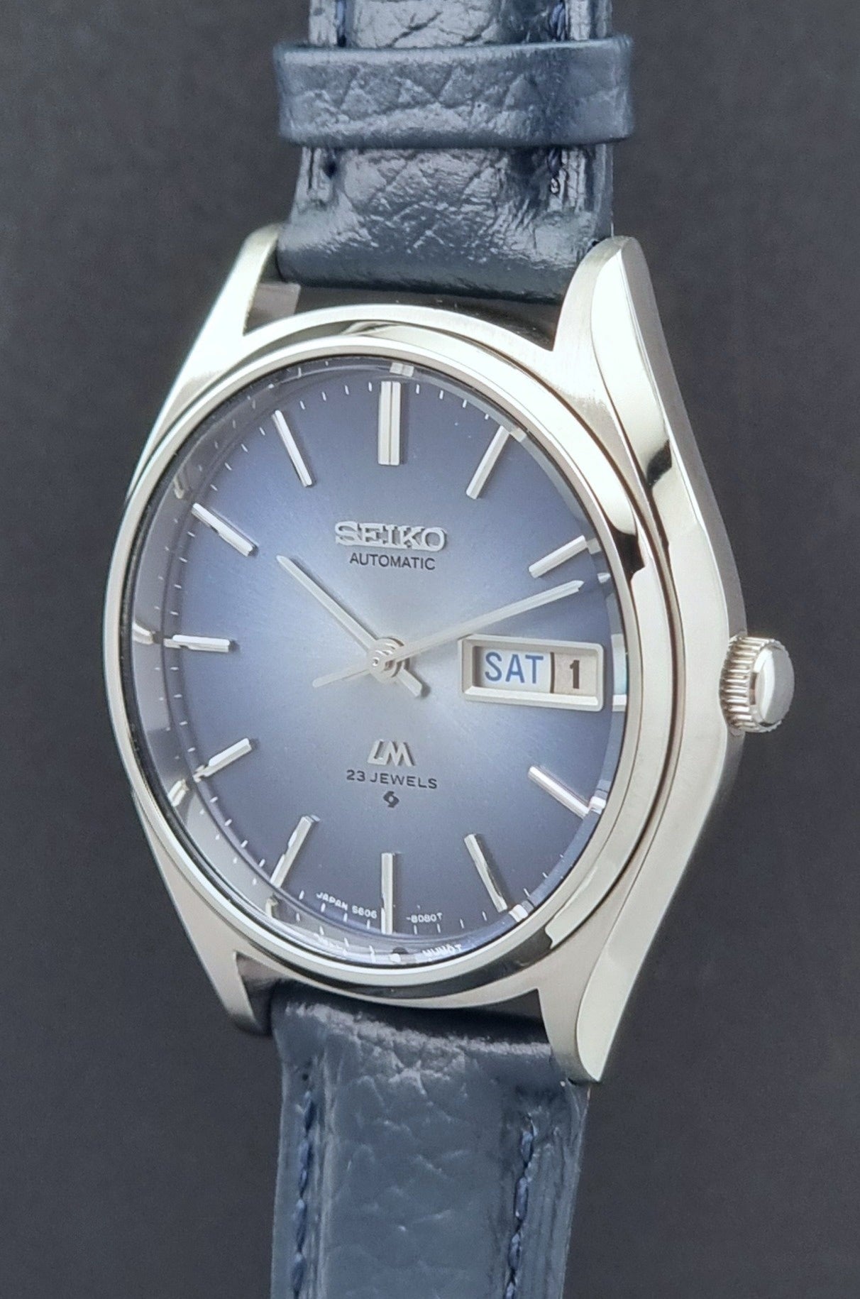 Vintage Seiko Wristwatch LordMatic 5606-8051 with blue strap with blue strap on a dark background blue dial crown side profile