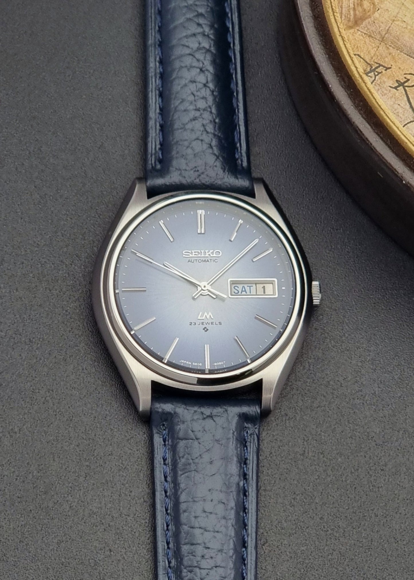 Vintage Seiko Wristwatch LordMatic 5606-8051 with blue strap with blue strap on a dark background front view