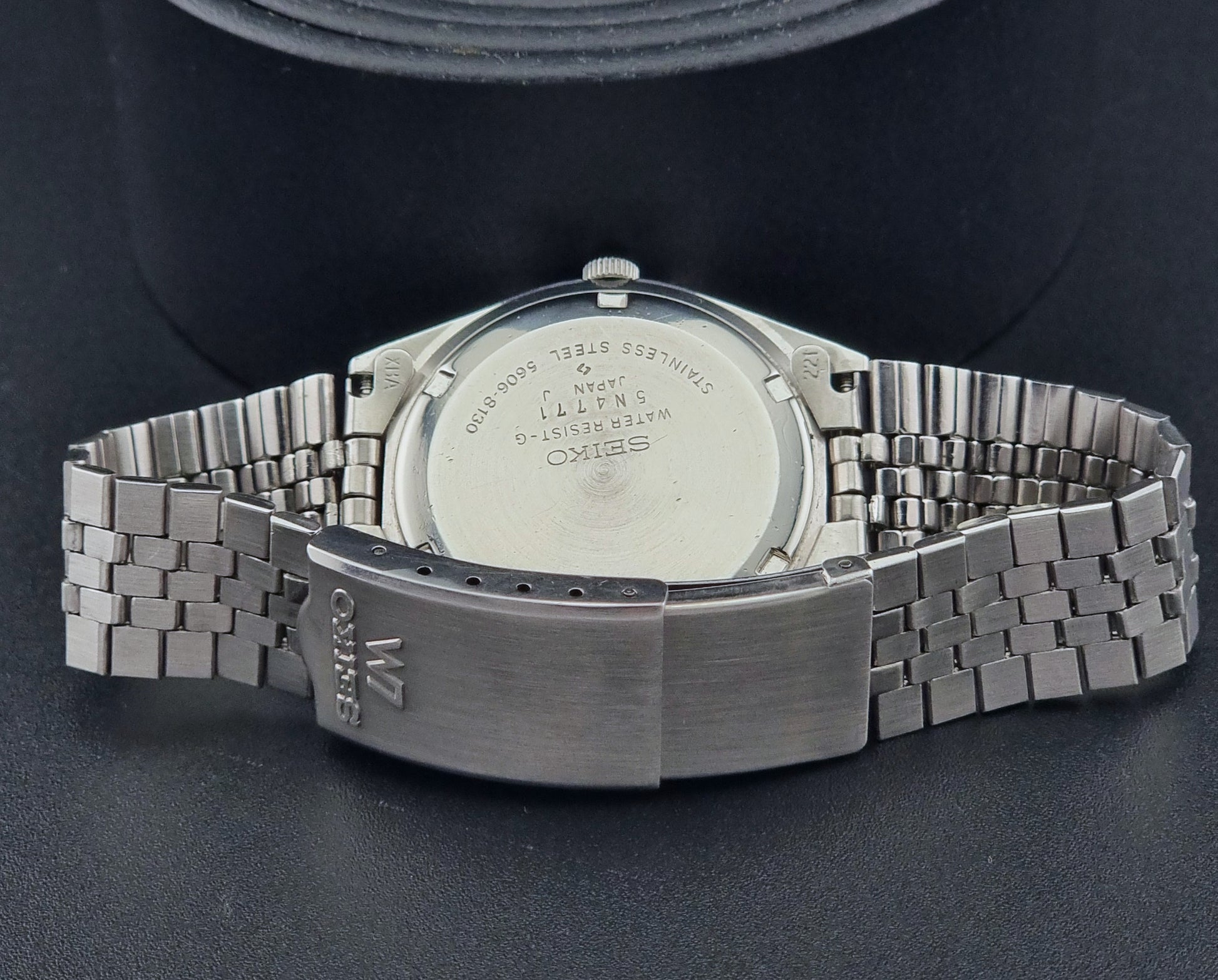 Vintage Seiko Lord Matic 56206-8130 watch with green face and silver metal strap on a dark textured background bracelet view