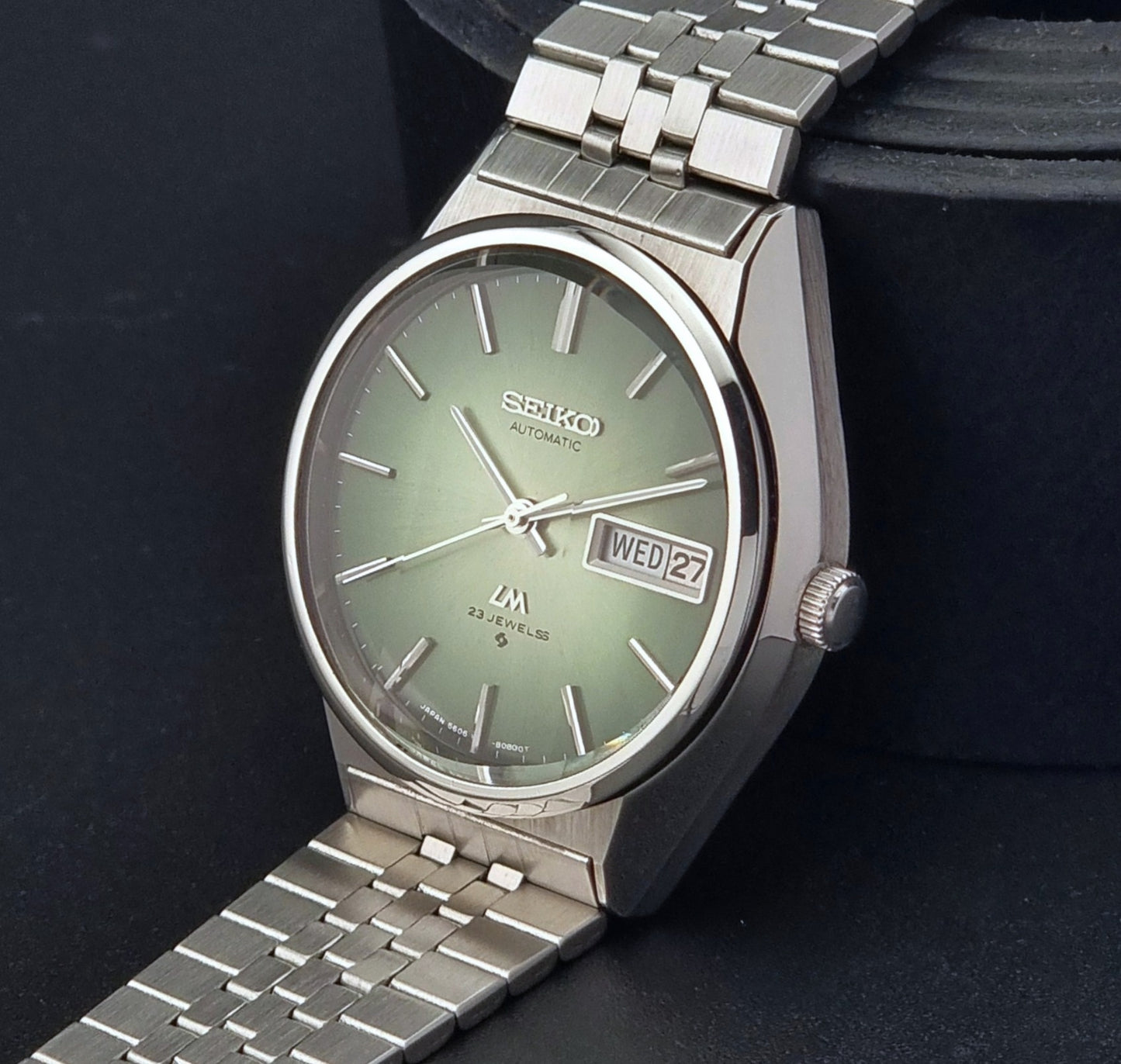 Vintage Seiko Lord Matic 56206-8130 watch with green face and silver metal strap on a dark textured background crown view