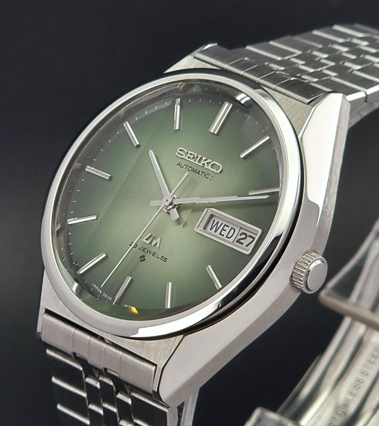 Vintage Seiko Lord Matic 56206-8130 watch with green face and silver metal strap on a dark textured background close up crown