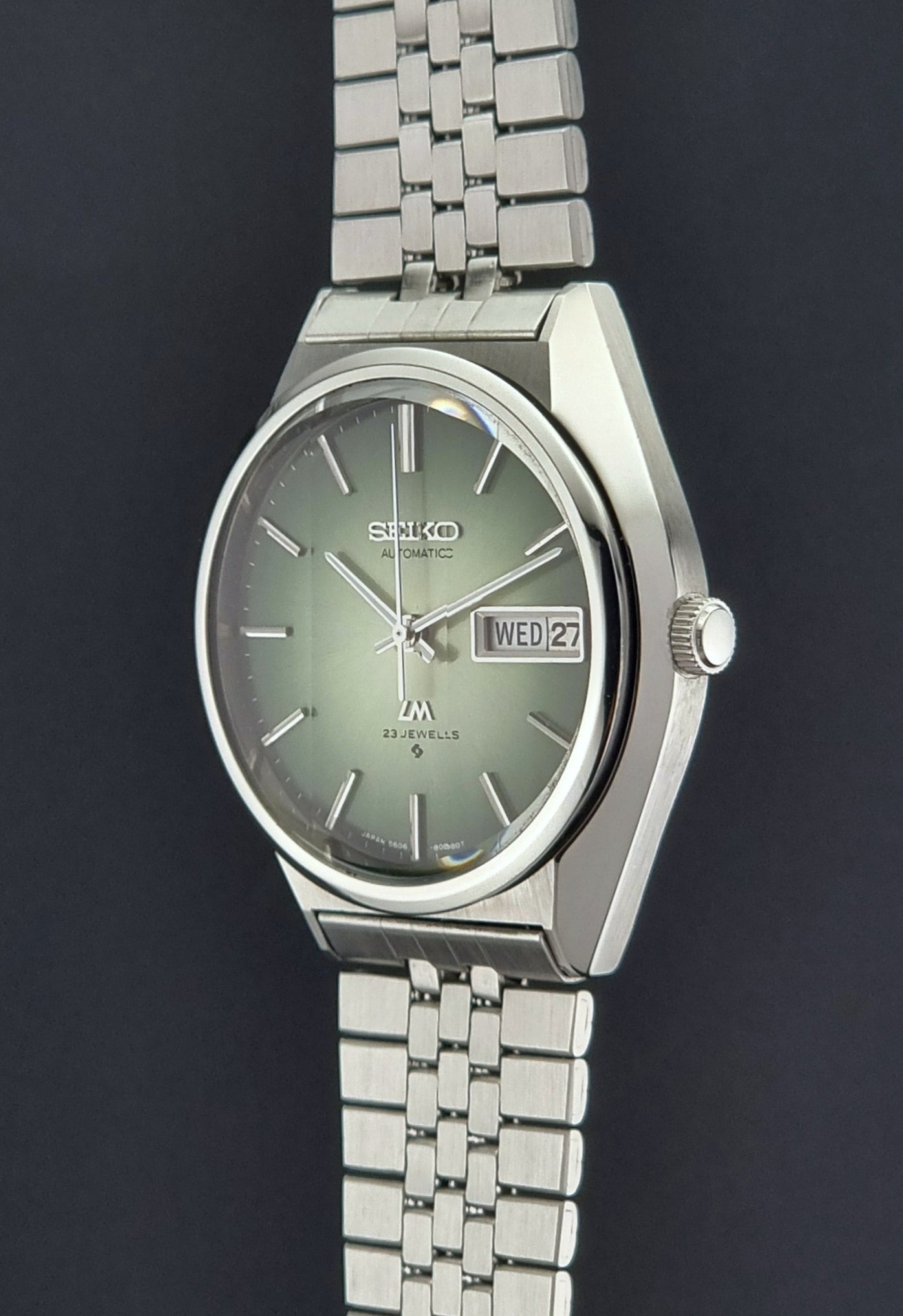 Vintage Seiko Lord Matic 56206-8130 watch with green face and silver metal strap on a dark textured background crown profile