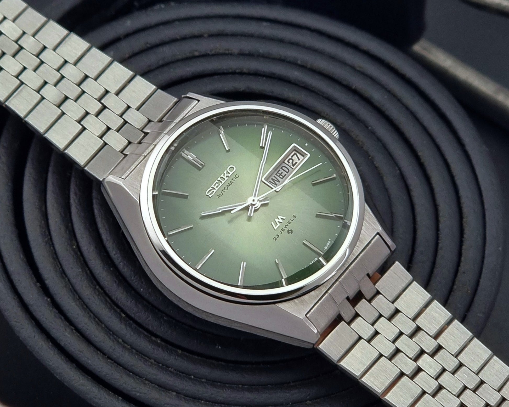 Vintage Seiko Lord Matic 56206-8130 watch with green face and silver metal strap on a dark textured background