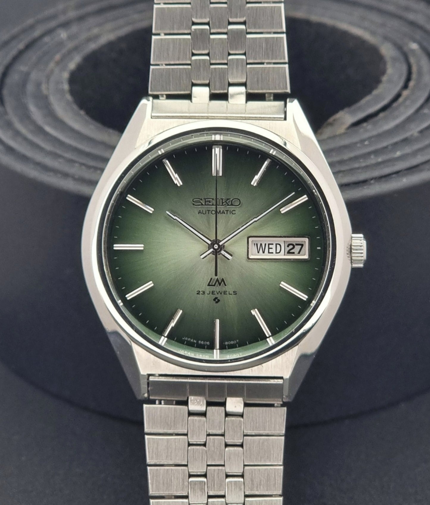 Vintage Seiko Lord Matic 56206-8130 watch with green face and silver metal strap on a dark textured background close up dial view