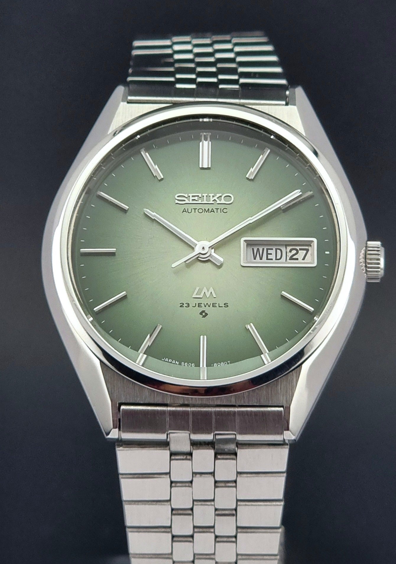 Vintage Seiko Lord Matic 56206-8130 watch with green face and silver metal strap on a dark textured background dial view