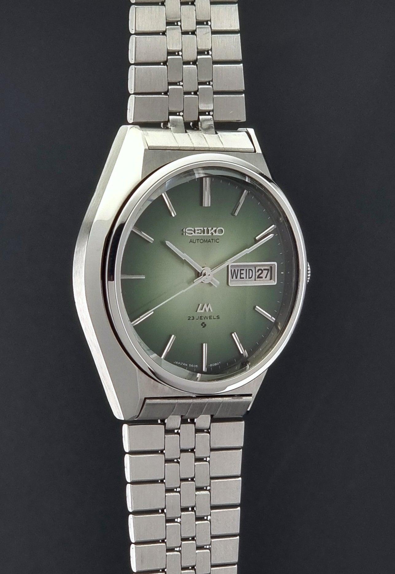Vintage Seiko Lord Matic 56206-8130 watch with green face and silver metal strap on a dark textured background side profile
