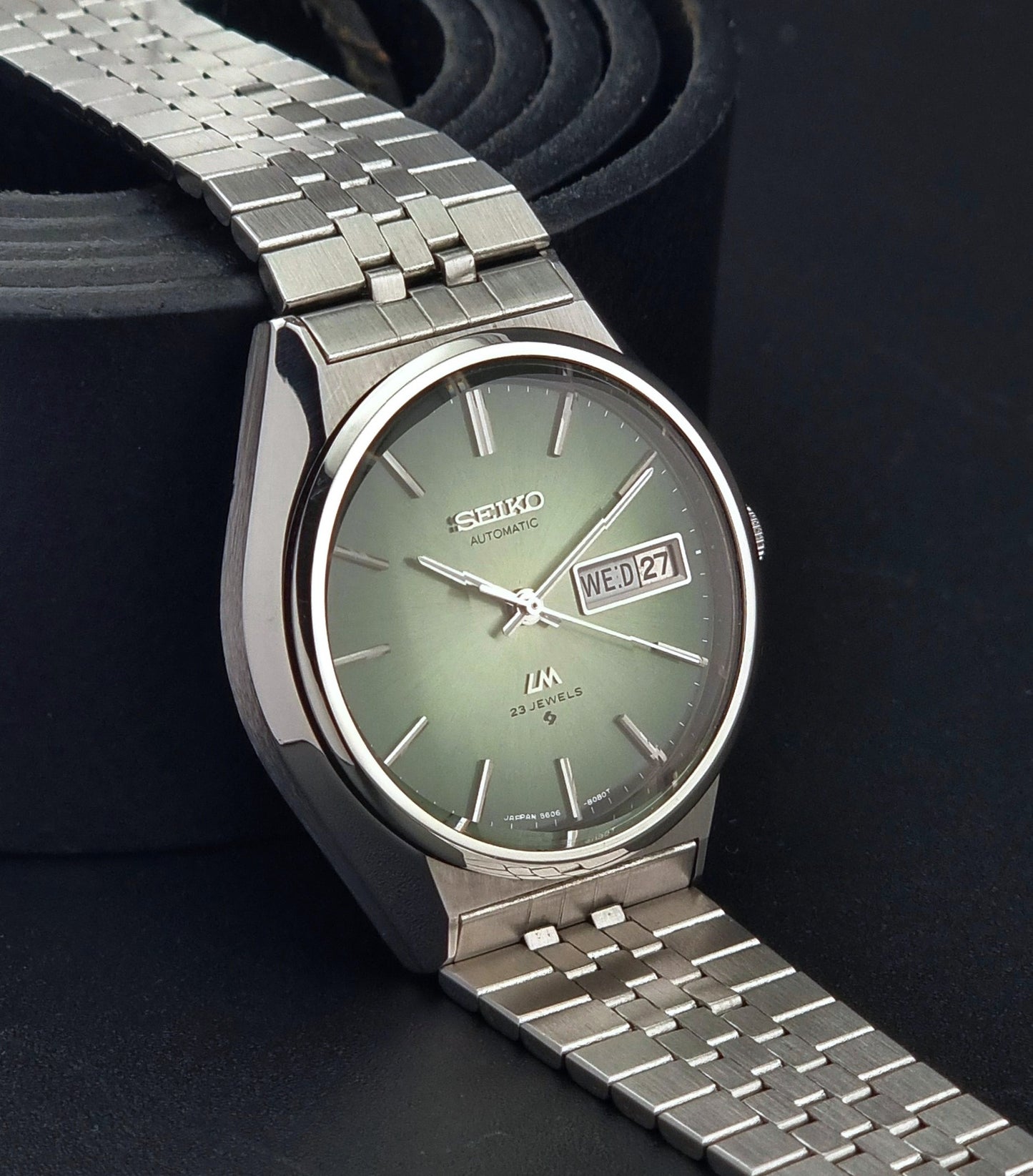 Vintage Seiko Lord Matic 56206-8130 watch with green face and silver metal strap on a dark textured background side view