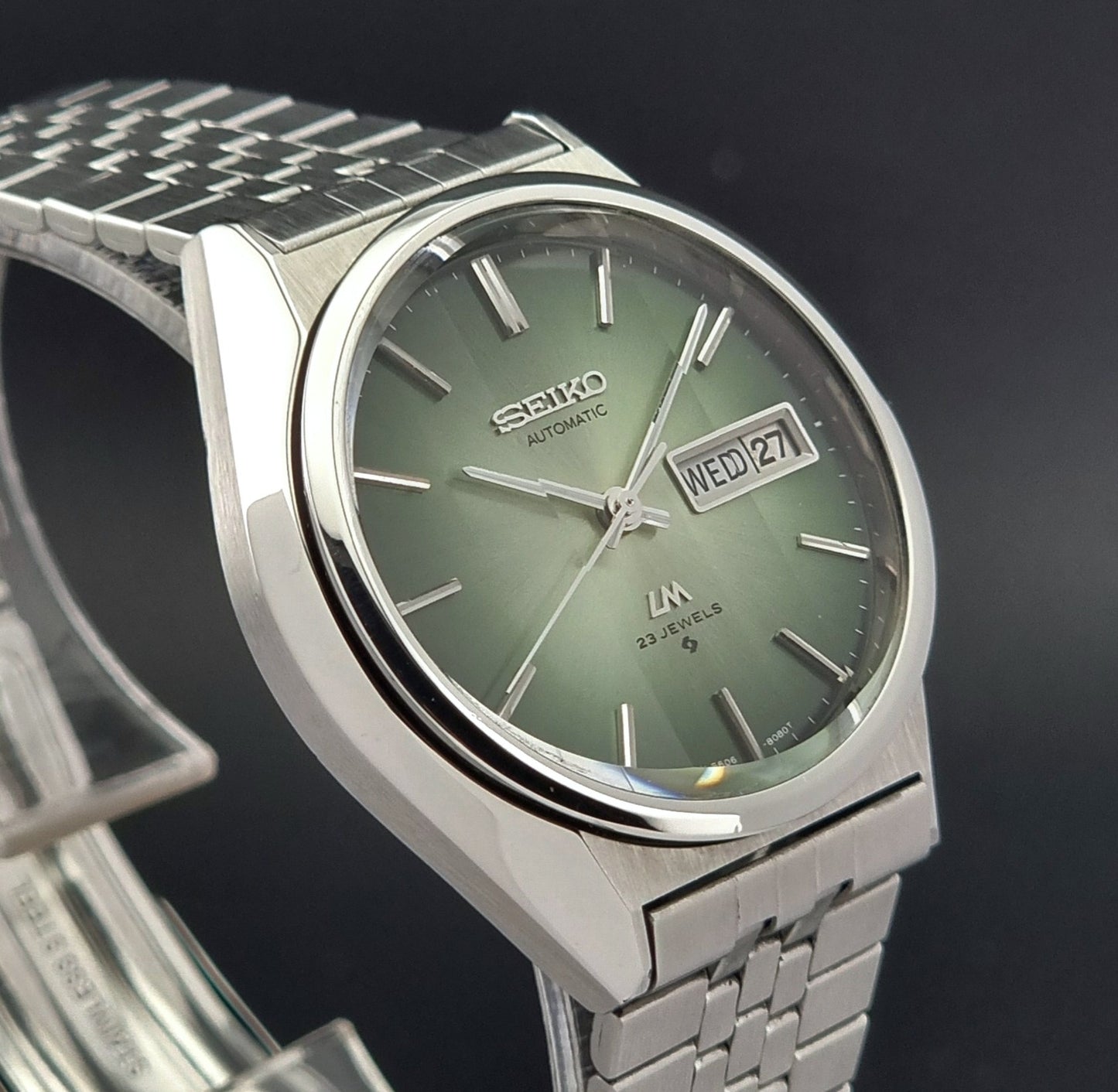 Vintage Seiko Lord Matic 56206-8130 watch with green face and silver metal strap on a dark textured background close up side
