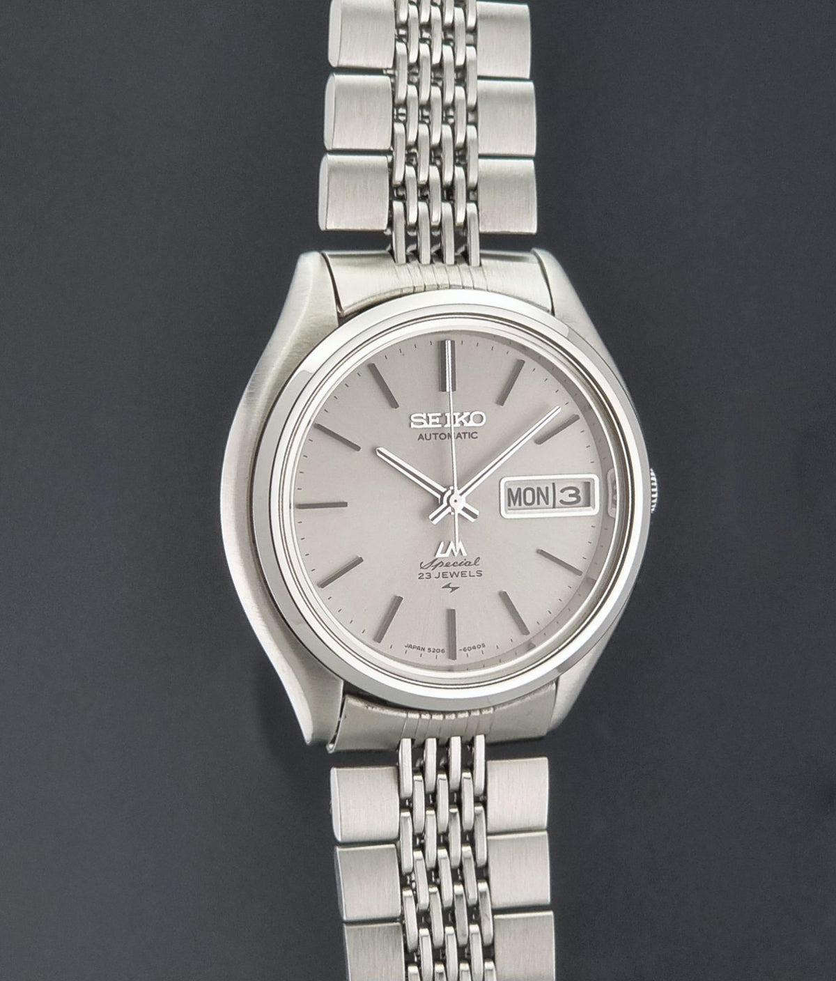 Vintage Seiko watch LordMatic Special 5206-6060 featuring a silver-toned stainless steel case and a matching silver dial with a day and date window, paired with a multi-link stainless steel bracelet, set against a dark gray background.