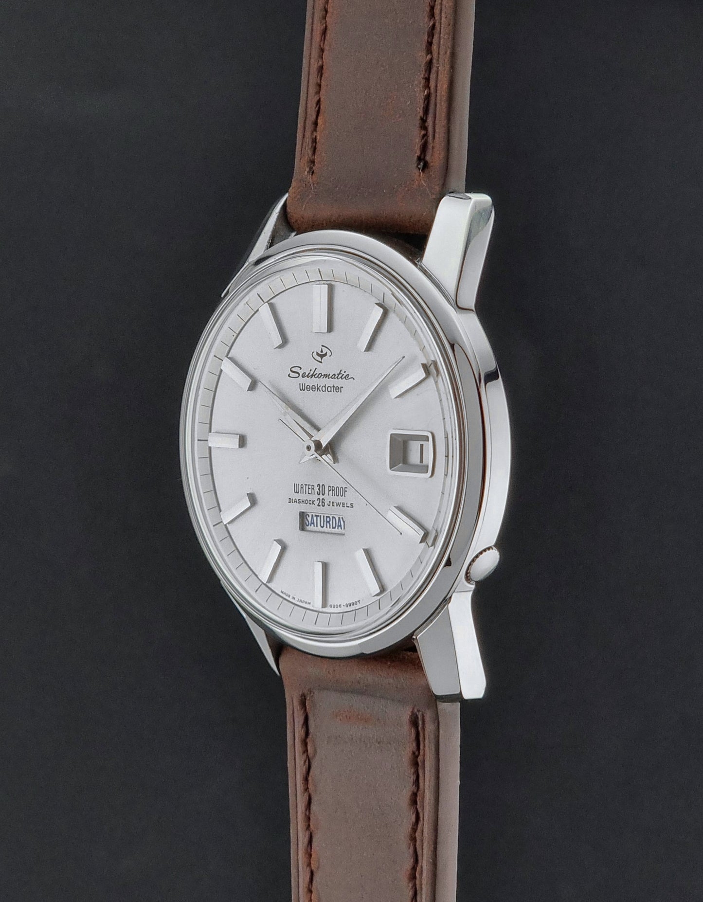 Vintage Seiko watch Seikomatic Weekdater 6206-8990 with brown leather strap on a gray textured background crown profile view