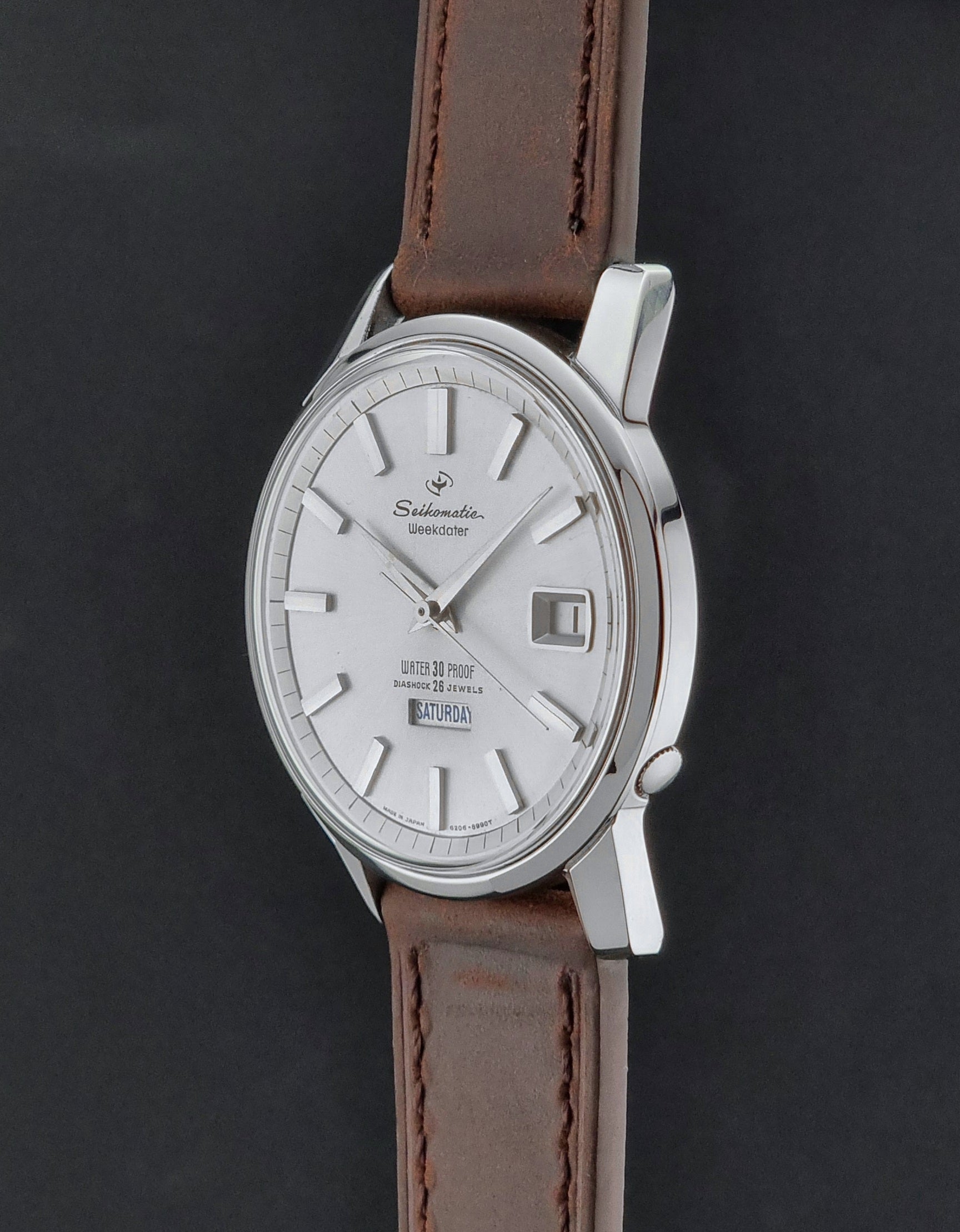 Vintage Seiko watch Seikomatic Weekdater 6206-8990 with brown leather strap on a gray textured background crown profile view
