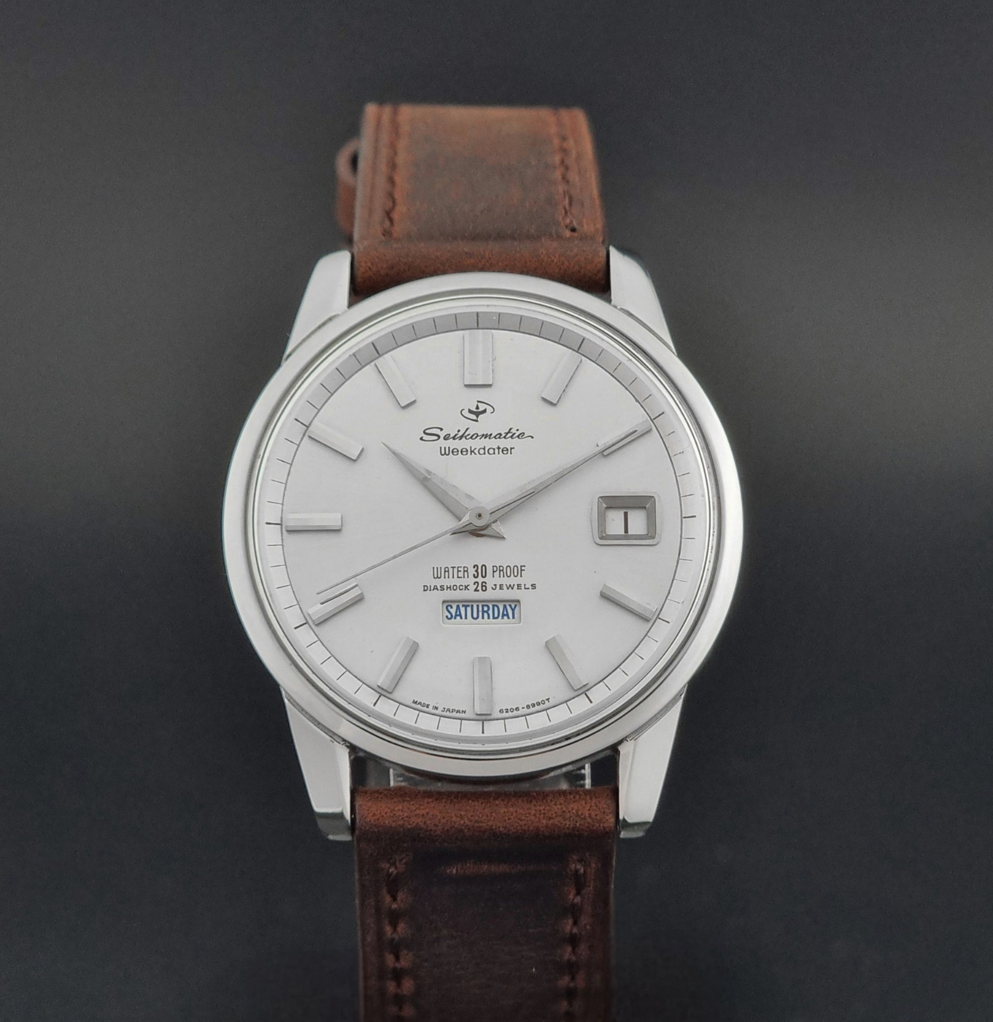 Vintage Seiko watch Seikomatic Weekdater 6206-8990 with brown leather strap on a gray textured background close up front