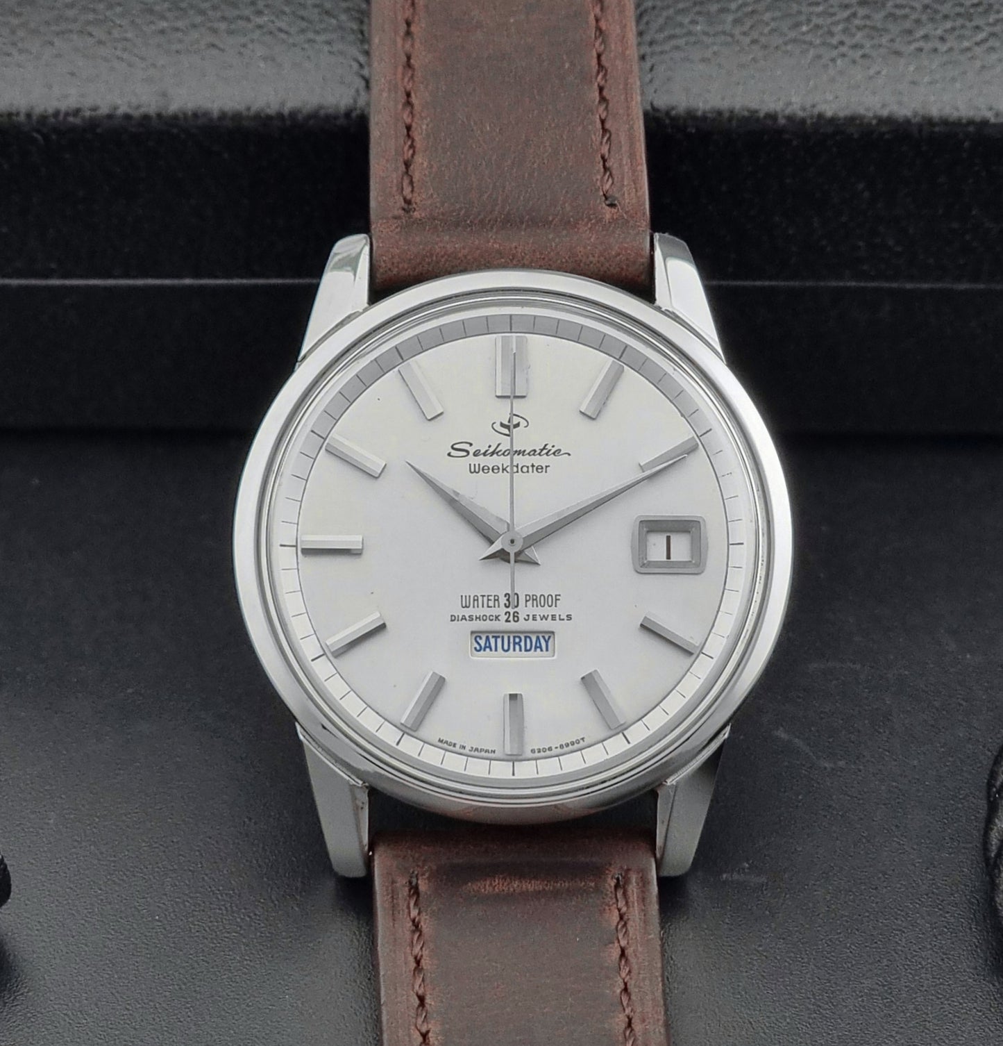 Vintage Seiko watch Seikomatic Weekdater 6206-8990 with brown leather strap on a gray textured background front view