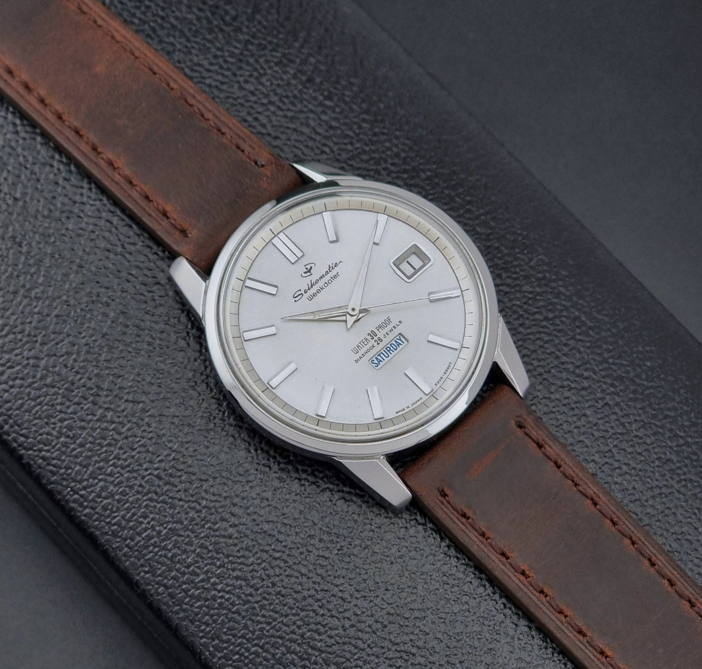Vintage Seiko watch Seikomatic Weekdater 6206-8990 with brown leather strap on a gray textured background front