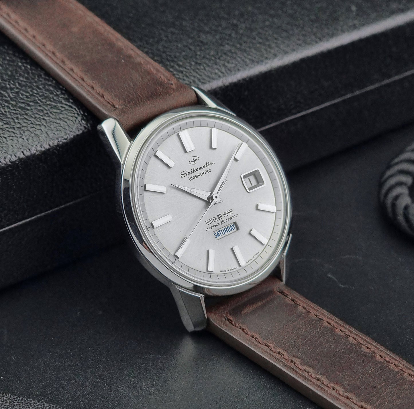Vintage Seiko watch Seikomatic Weekdater 6206-8990 with brown leather strap on a gray textured background side view
