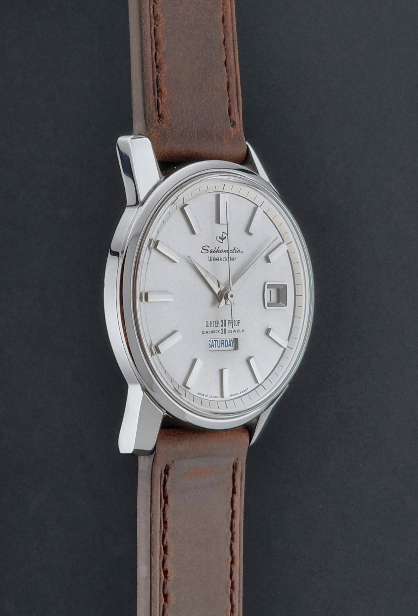 Vintage Seiko watch Seikomatic Weekdater 6206-8990 with brown leather strap on a gray textured background side profile view
