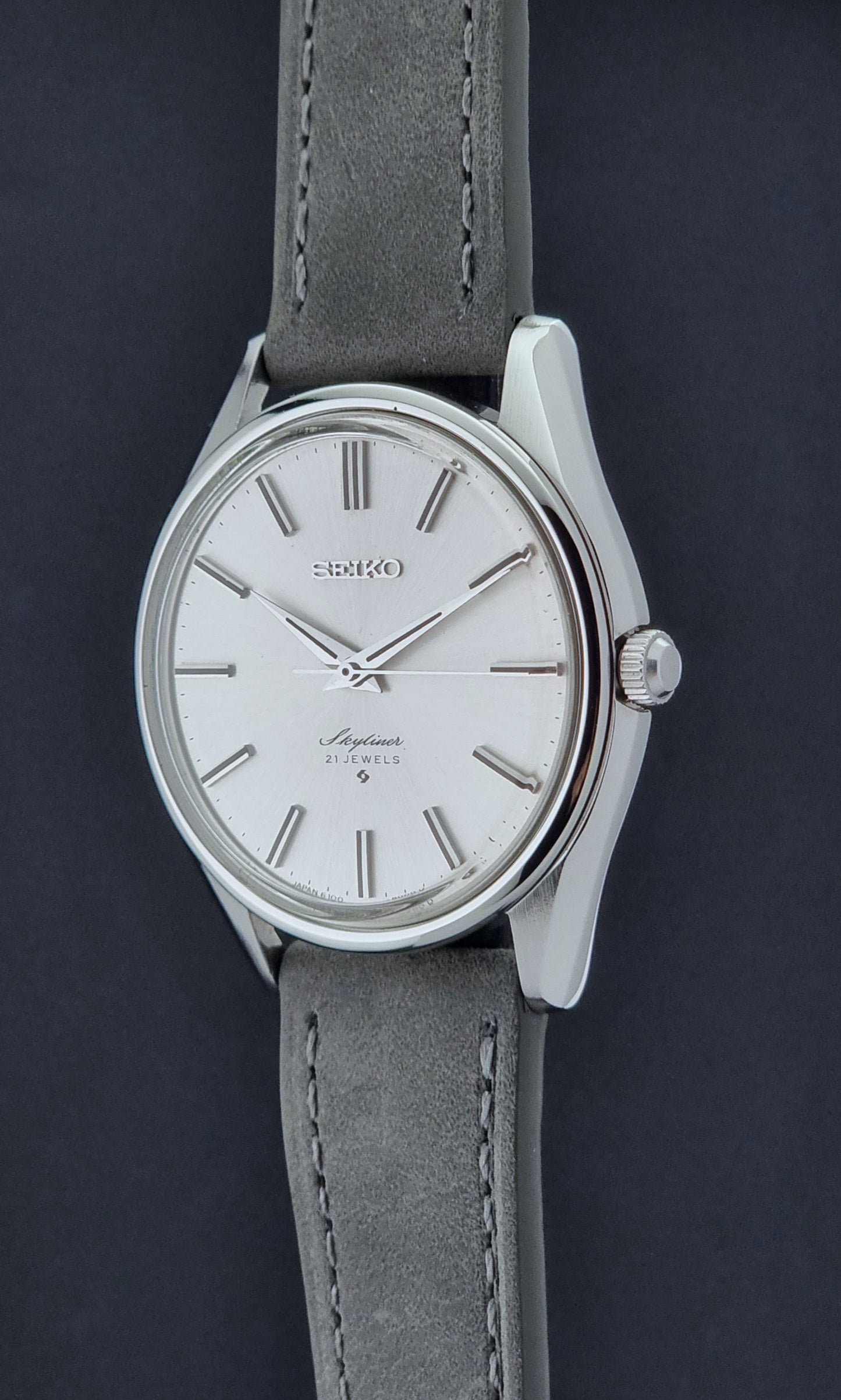 Vintage Seiko Wristwatch Skyliner 6100-8000 with a grey leather strap and silver case on a grey background crown profile view