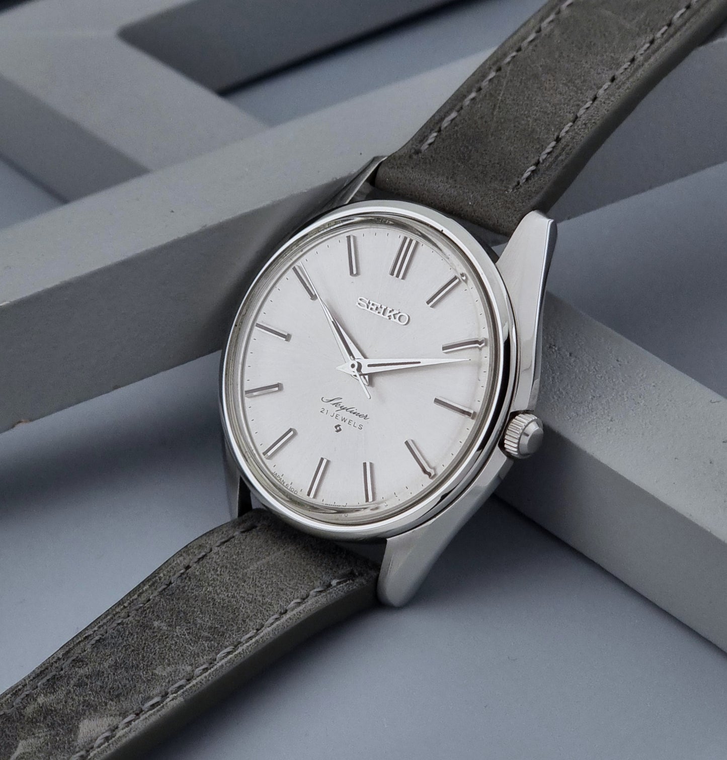 Vintage Seiko Wristwatch Skyliner 6100-8000 with a grey leather strap and silver case on a grey background crown view