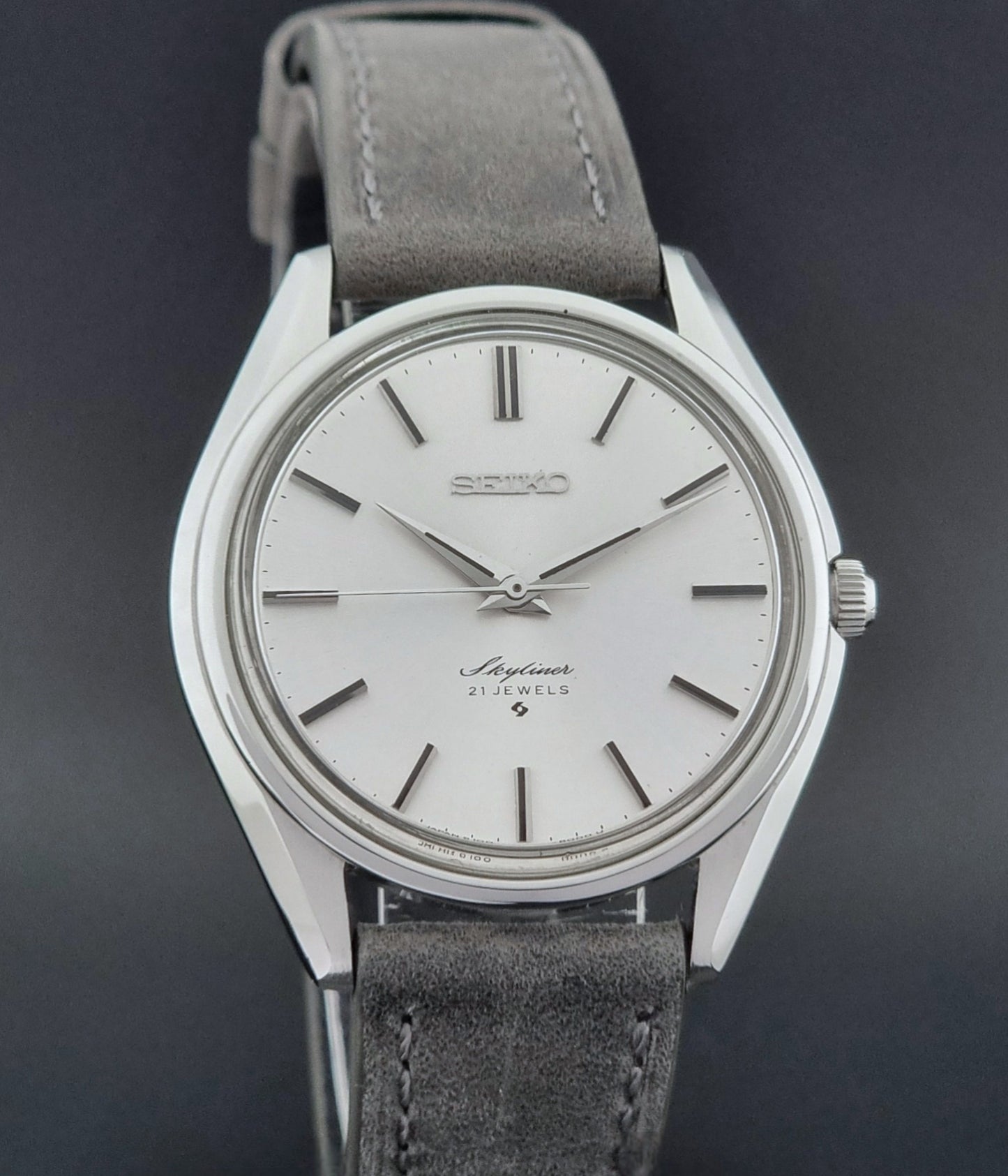 Vintage Seiko Wristwatch Skyliner 6100-8000 with a grey leather strap and silver case on a grey background close front view