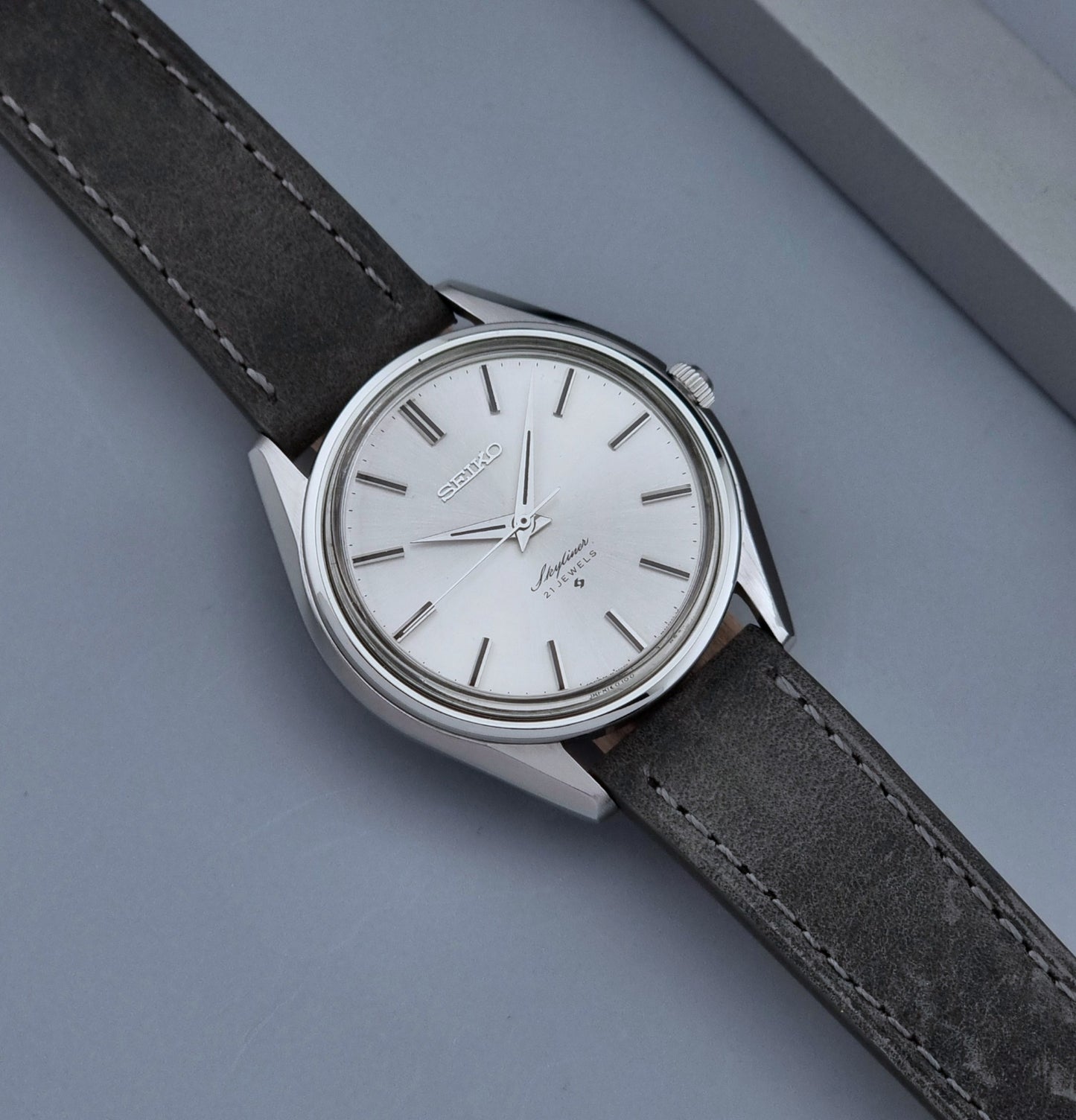 Vintage Seiko Wristwatch Skyliner 6100-8000 with a grey leather strap and silver case on a grey background front