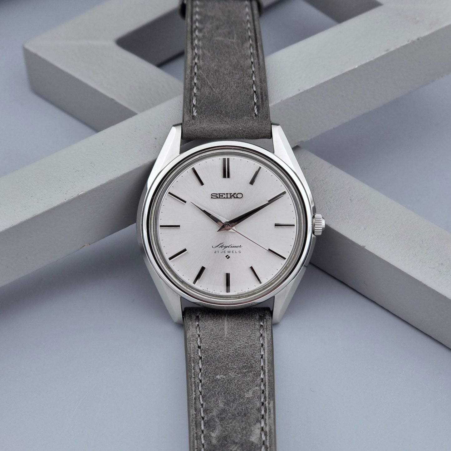 Vintage Seiko Wristwatch Skyliner 6100-8000 with a grey leather strap and silver case on a grey back ground front view