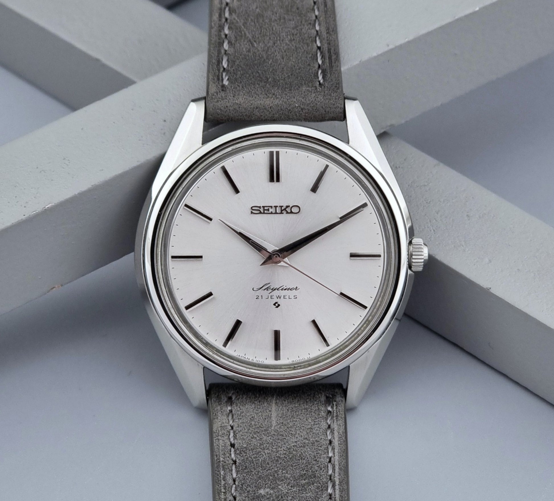 Vintage Seiko Wristwatch Skyliner 6100-8000 with a grey leather strap and silver case on a grey background close up dial view