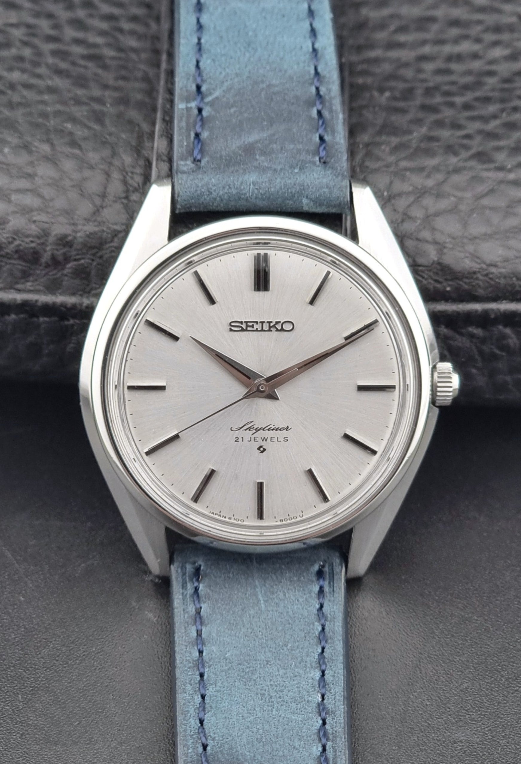 Seiko Skyliner 6100-8000 watch with a silver case and light blue leather strap on a textured gray background