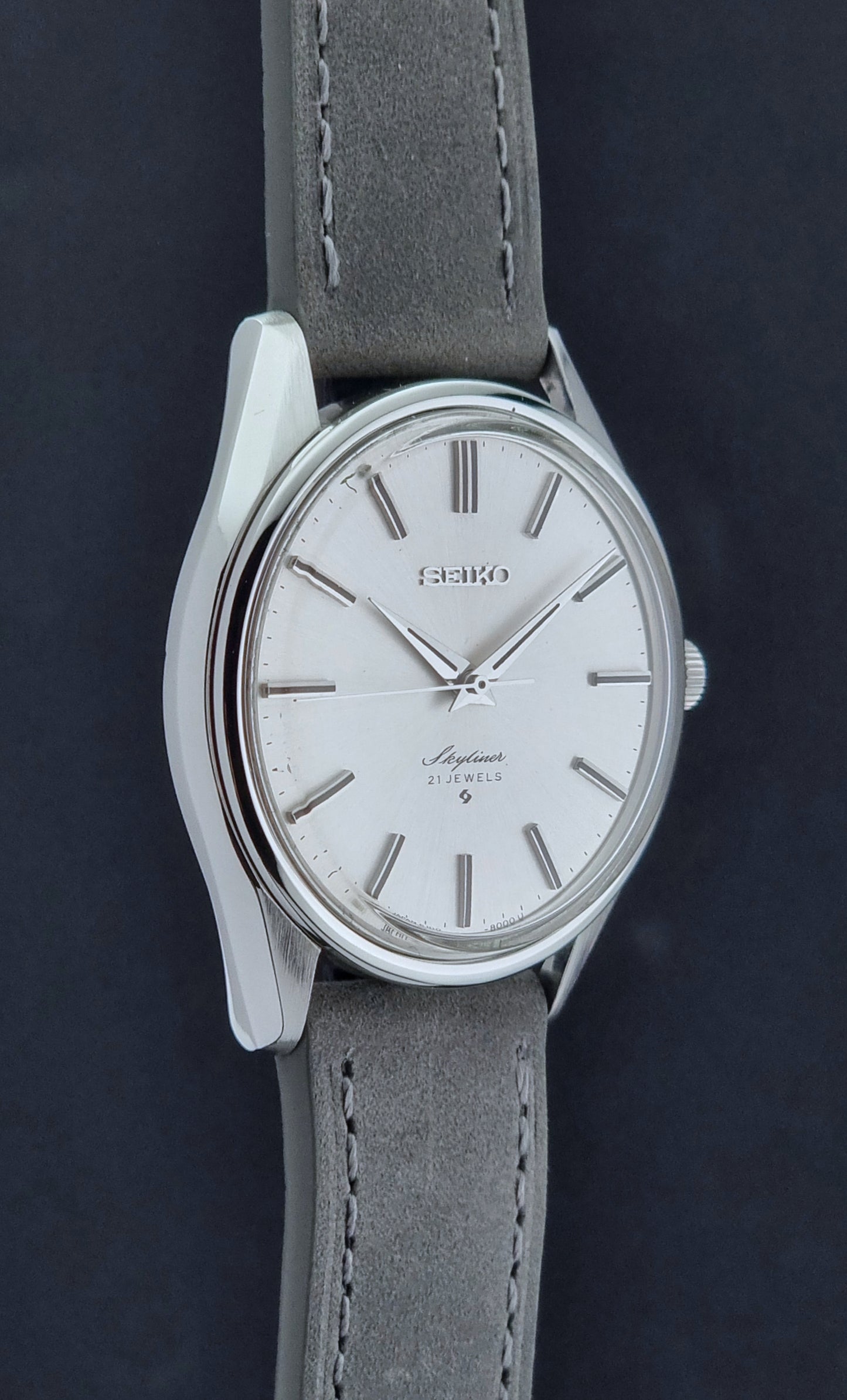 Vintage Seiko Wristwatch Skyliner 6100-8000 with a grey leather strap and silver case on a grey background side profile view